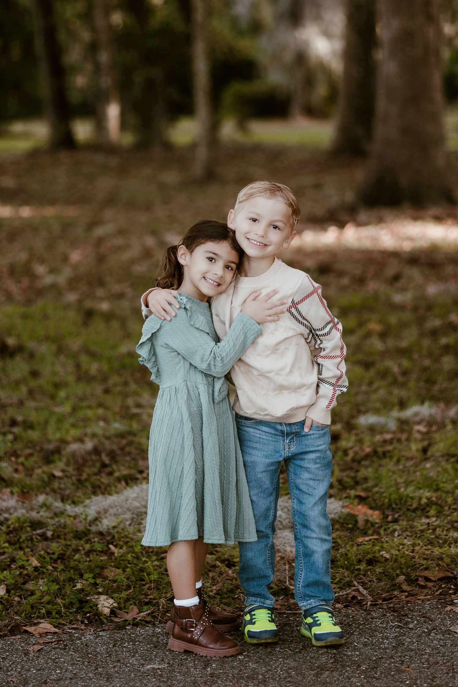 Two small children in casual wear hugging and posing together on a woodland path.