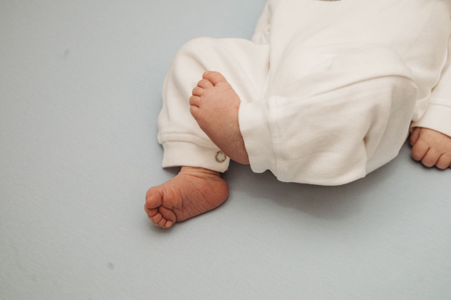 Close-up details of tiny baby feet in white clothing against light background.