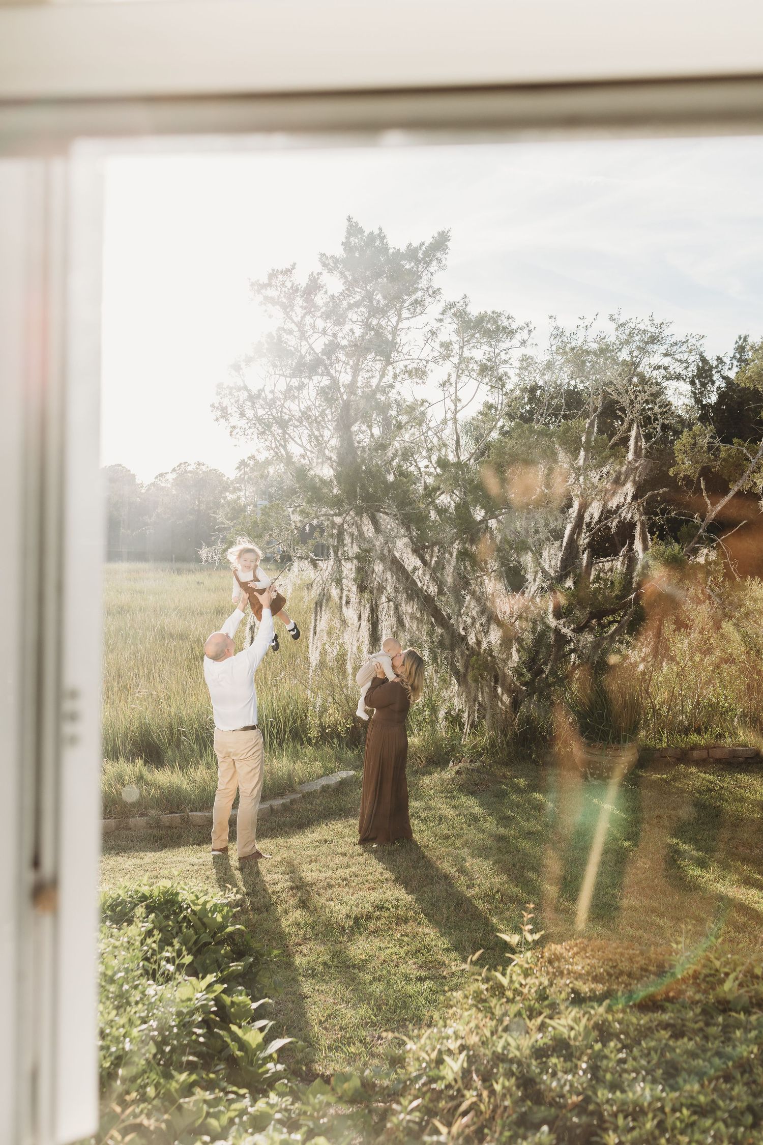 A couple plays and dances together in a sunlit garden with Spanish moss hanging from trees.