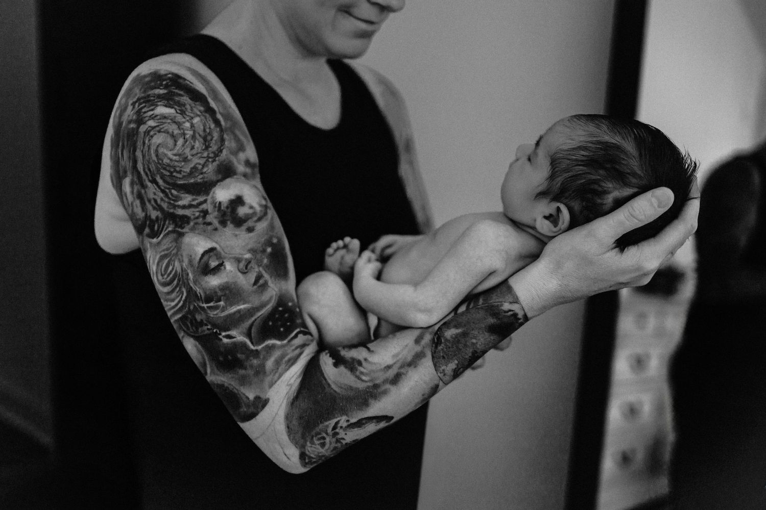 Black and white photo showing tender interaction between parent and newborn baby in intimate close-up.