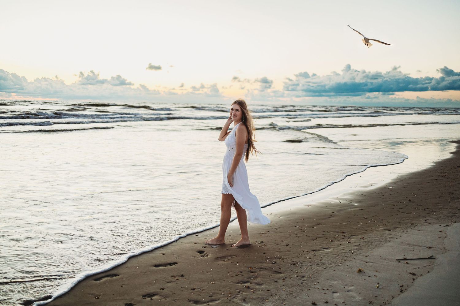 A figure walks along a scenic beach shoreline during sunset with waves crashing against the sand.