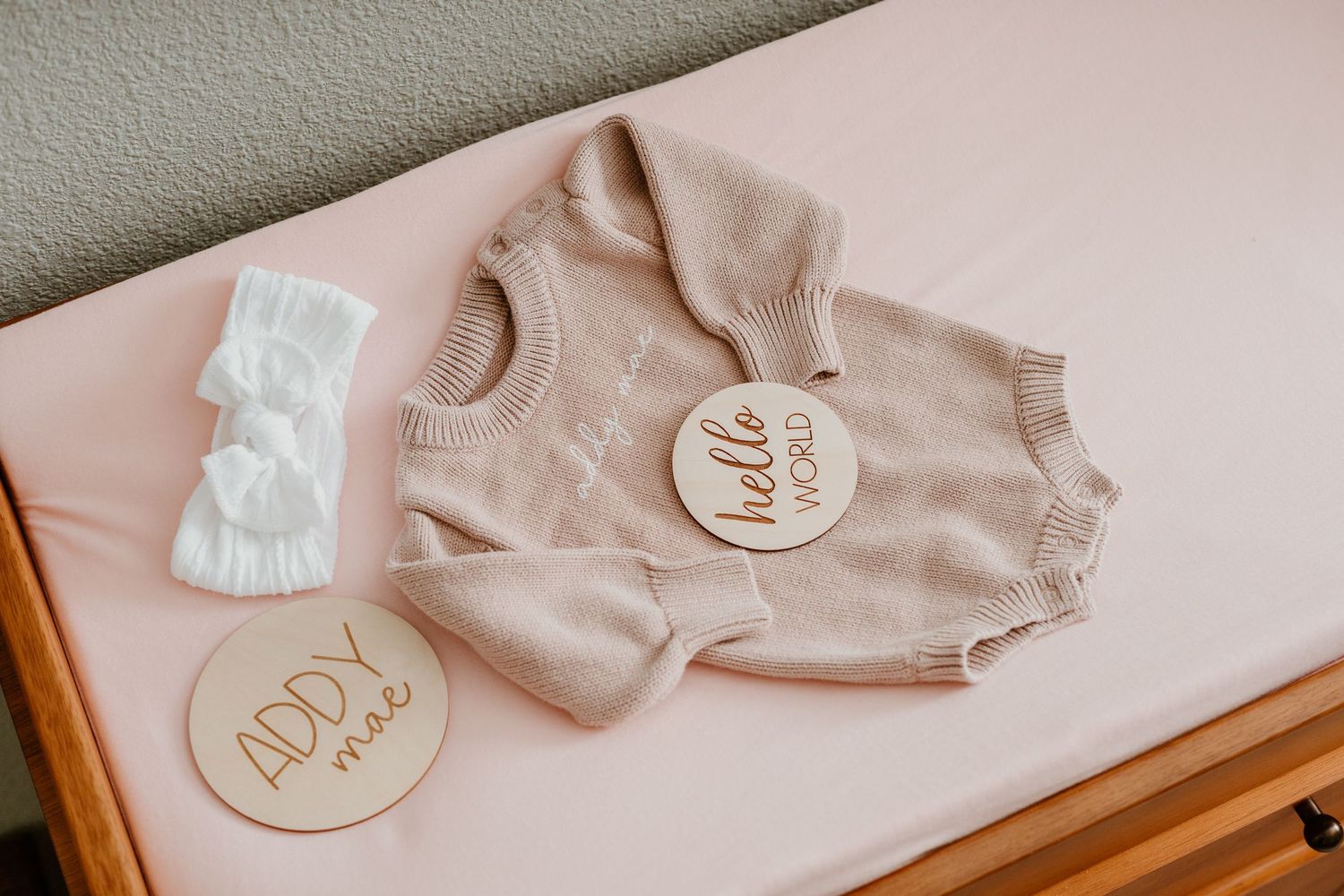 Soft pink baby clothing and accessories laid out on a neutral surface.
