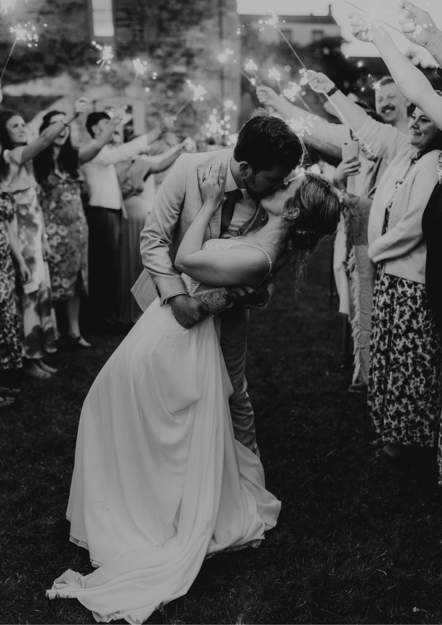 Black and white photo of a couple sharing a romantic dip kiss during a sparkler wedding send-off at priston mill in bath