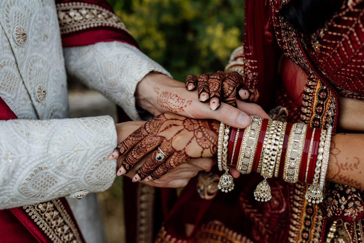 Hands adorned with traditional Indian bridal jewelry and henna display intricate bangles and rings during a wedding ceremony.