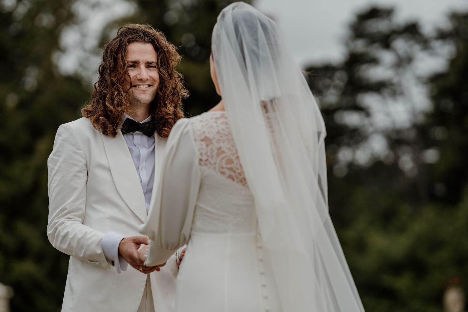 A groom in a white suit holds hands with a bride at orchardleigh house in wiltshire