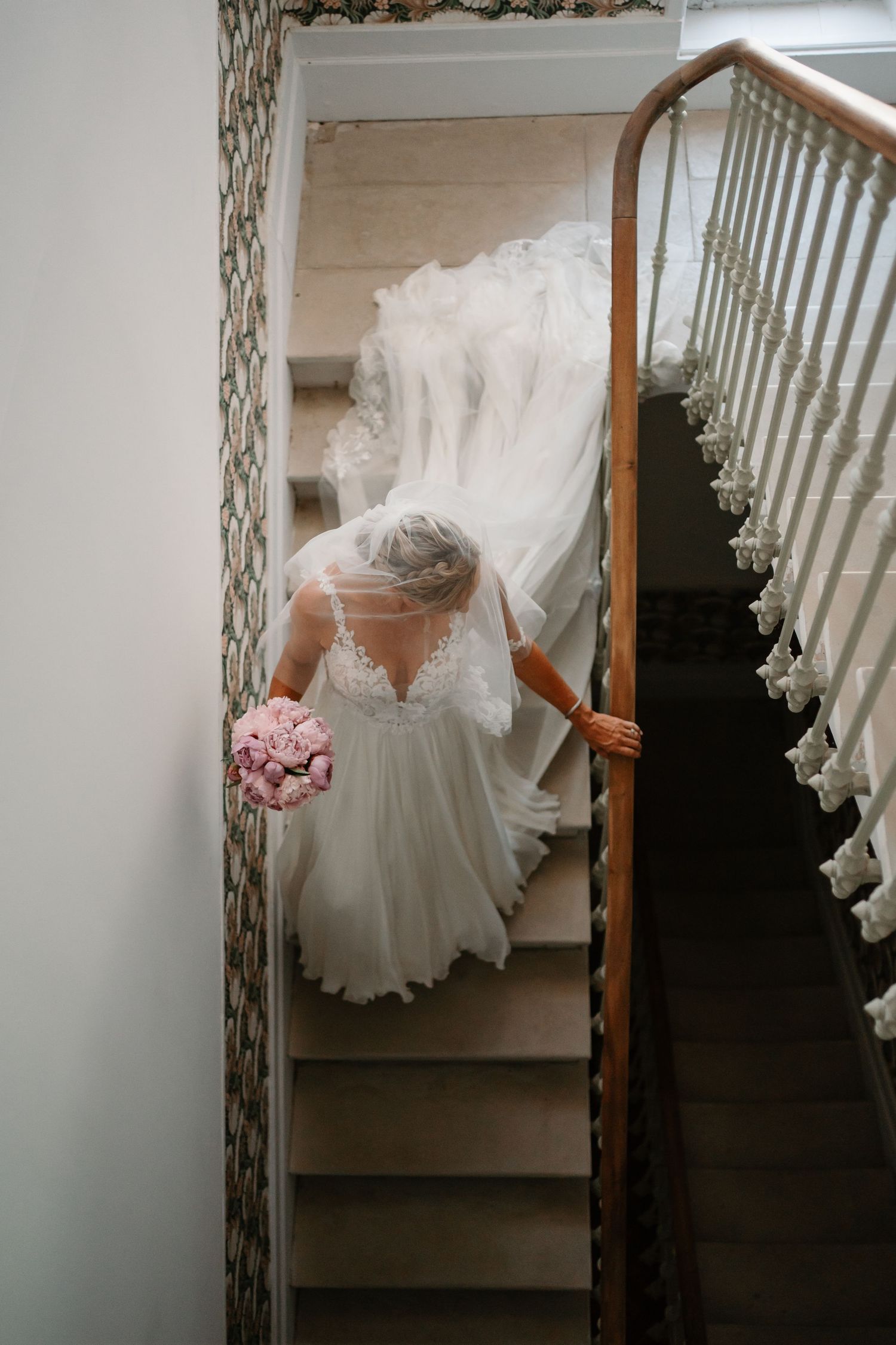 A white wedding dress with ruffled details hangs elegantly on a staircase railing in a home interior.