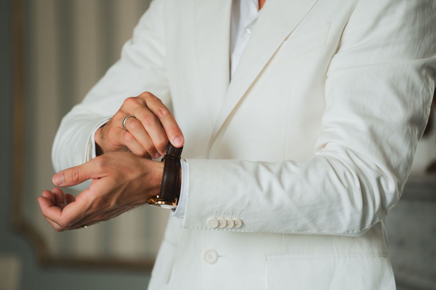 Close up view of hands adjusting a white dress shirt sleeve button against a blurred background.