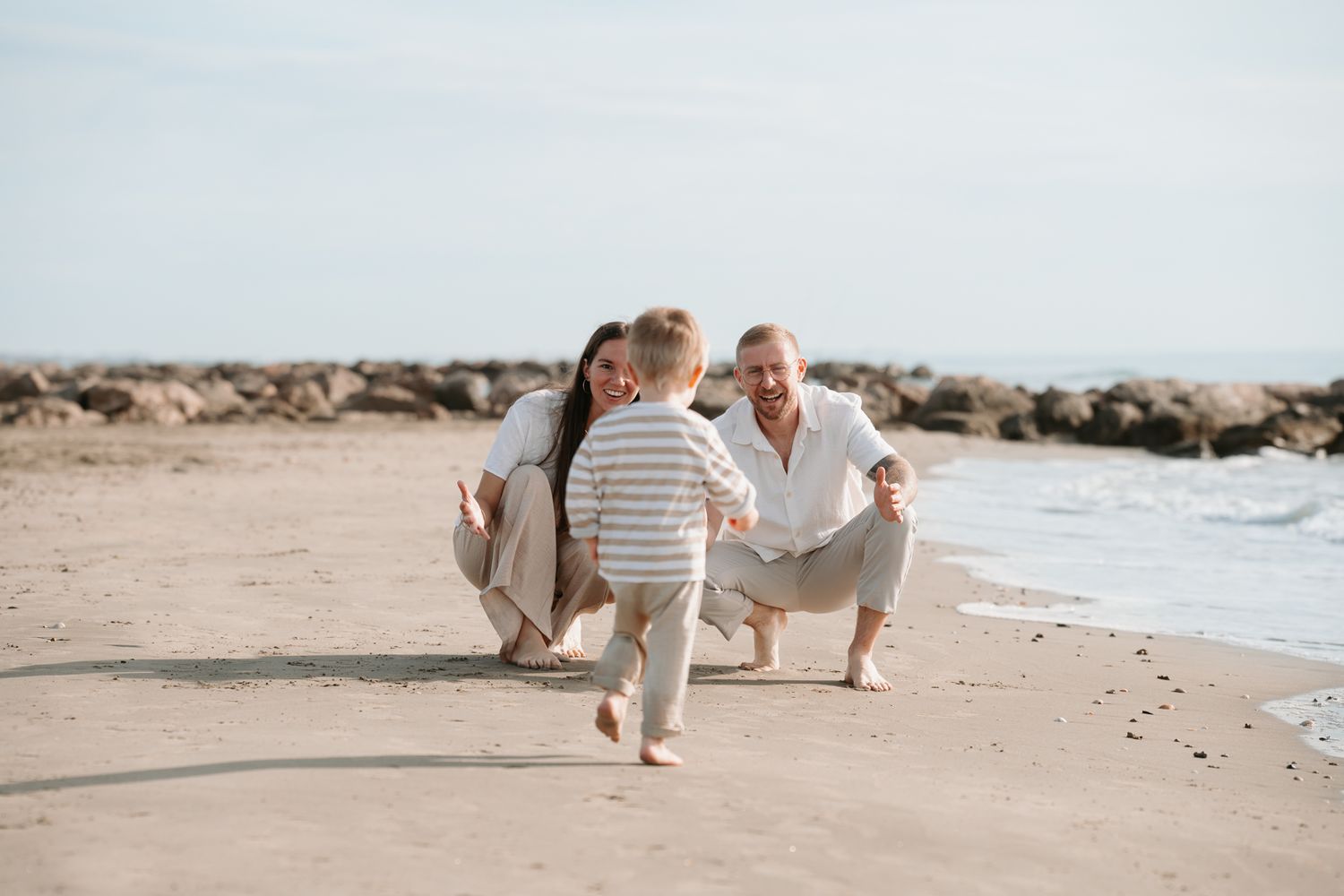 Two people in light clothing walk along a sandy beach with ocean waves in the background.
