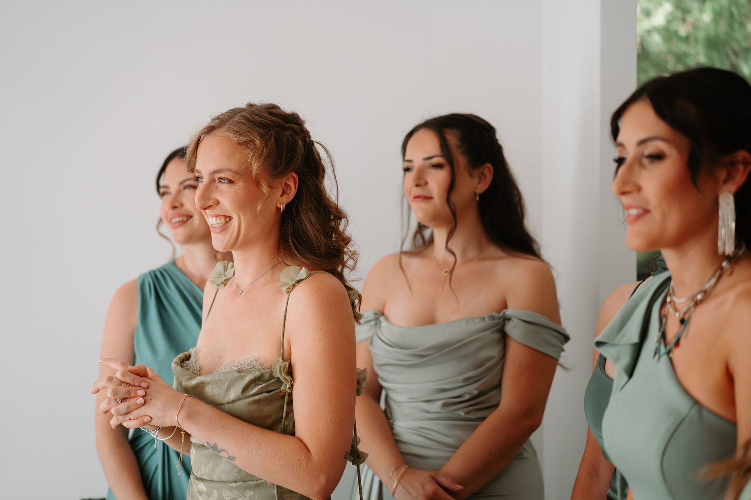 Bridesmaids in sage green dresses share a candid laughing moment during a wedding celebration.