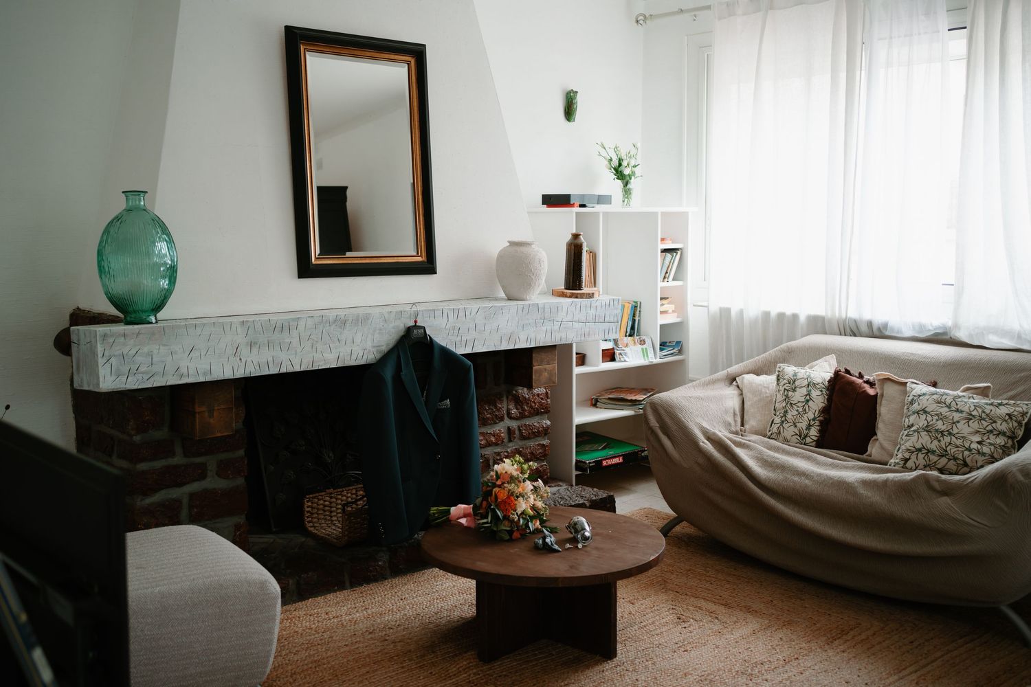 Cozy living room interior with brick fireplace, round coffee table, and white sofa near sheer curtained window.
