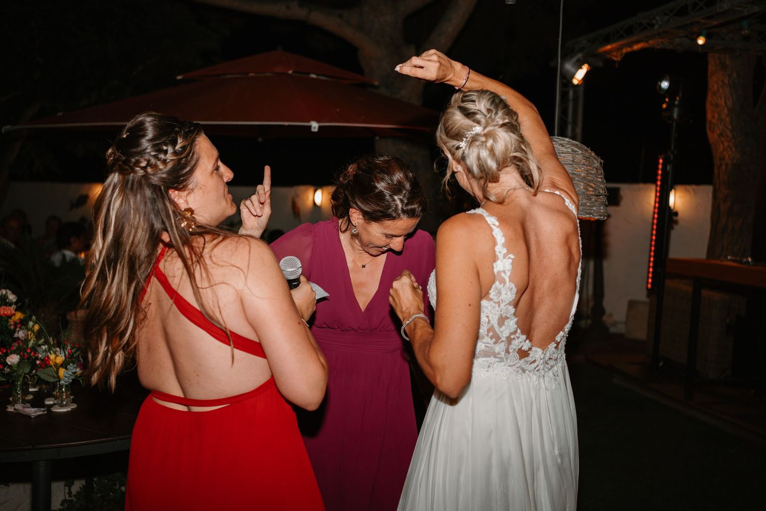 Three women in formal dresses share an emotional moment at an evening event.