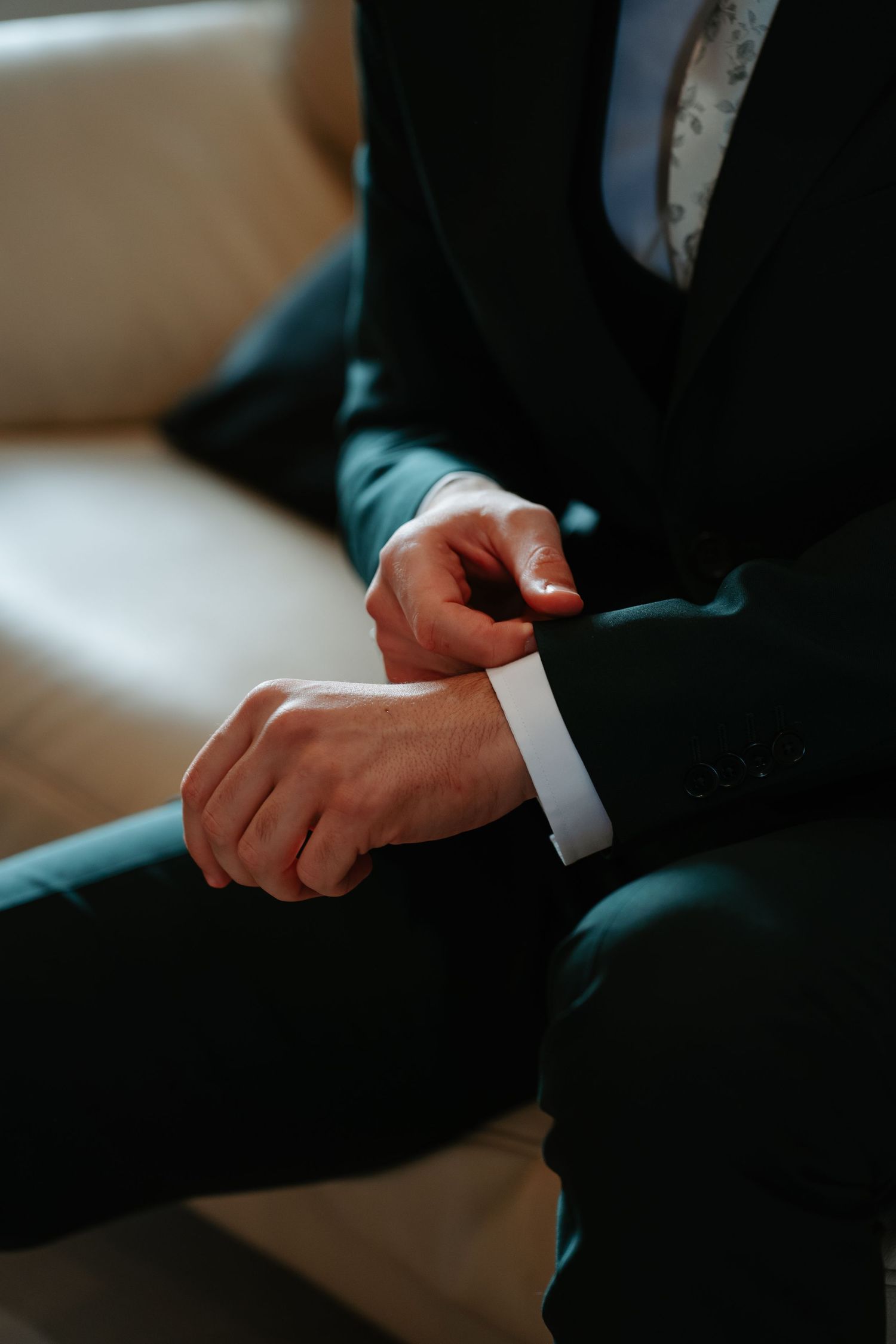 A close-up of hands adjusting a formal suit sleeve cuff in dark lighting.