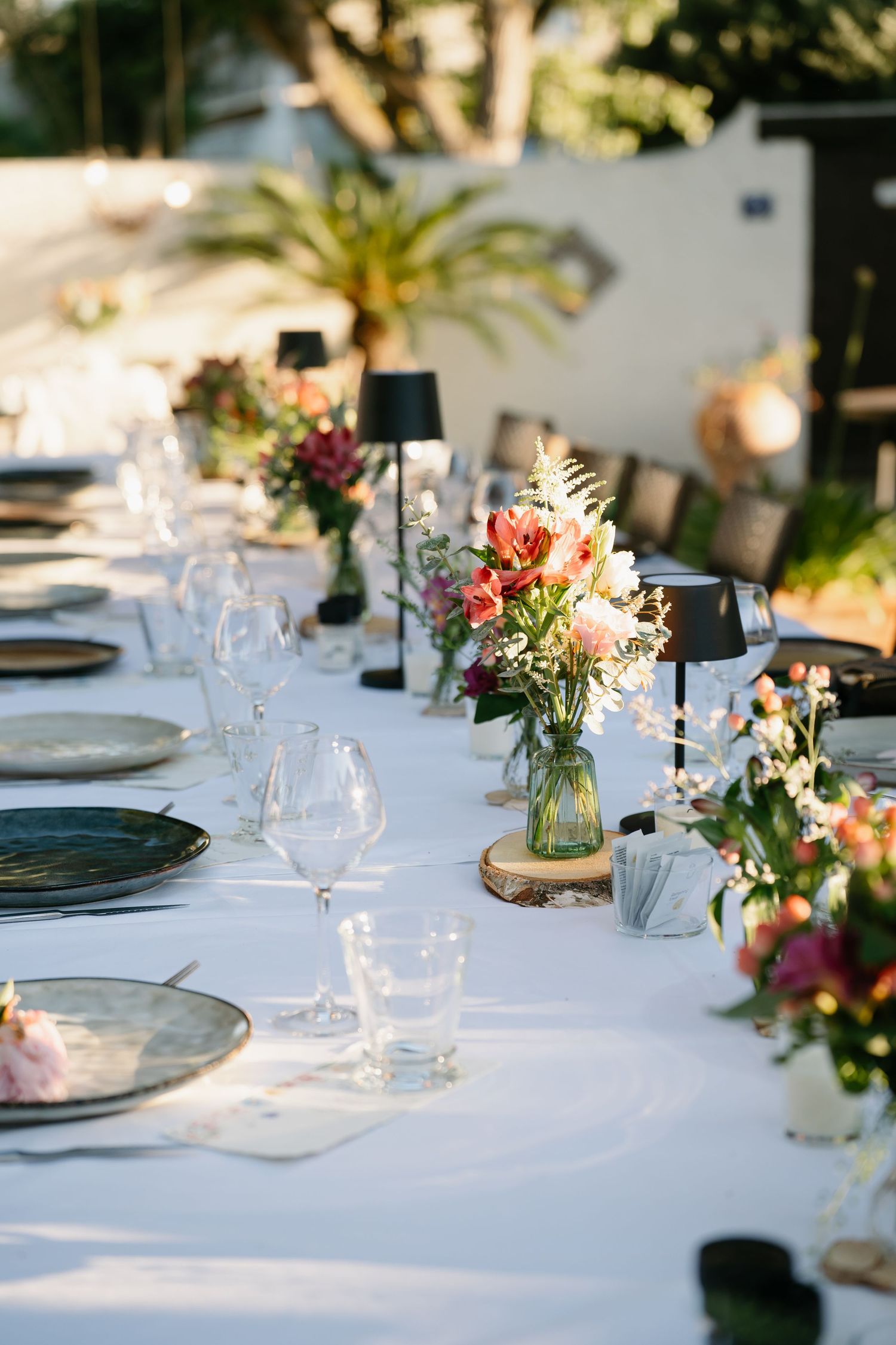 Elegant outdoor wedding reception table settings with white linens, rustic wood accents, and delicate floral centerpieces.