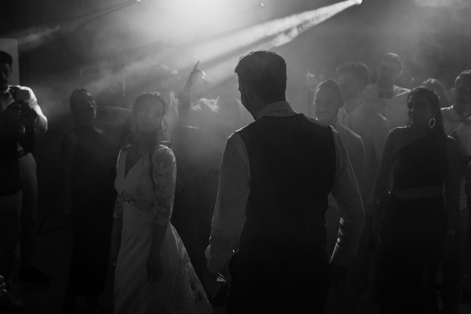 A silhouetted crowd of people dancing in a dark nightclub with atmospheric lighting and smoke effects.