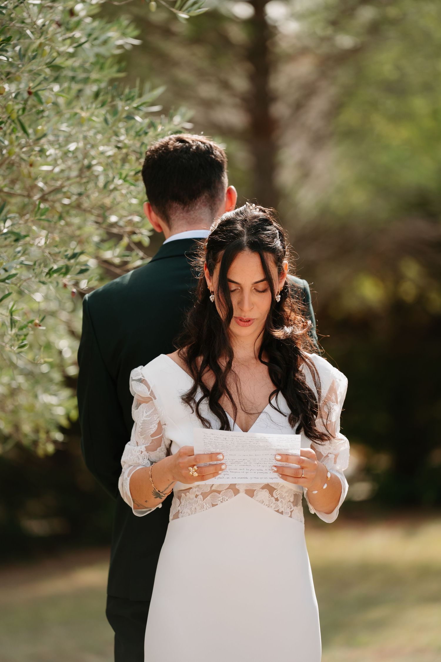 A romantic wedding scene in a garden setting shows a couple sharing an intimate moment among olive trees.