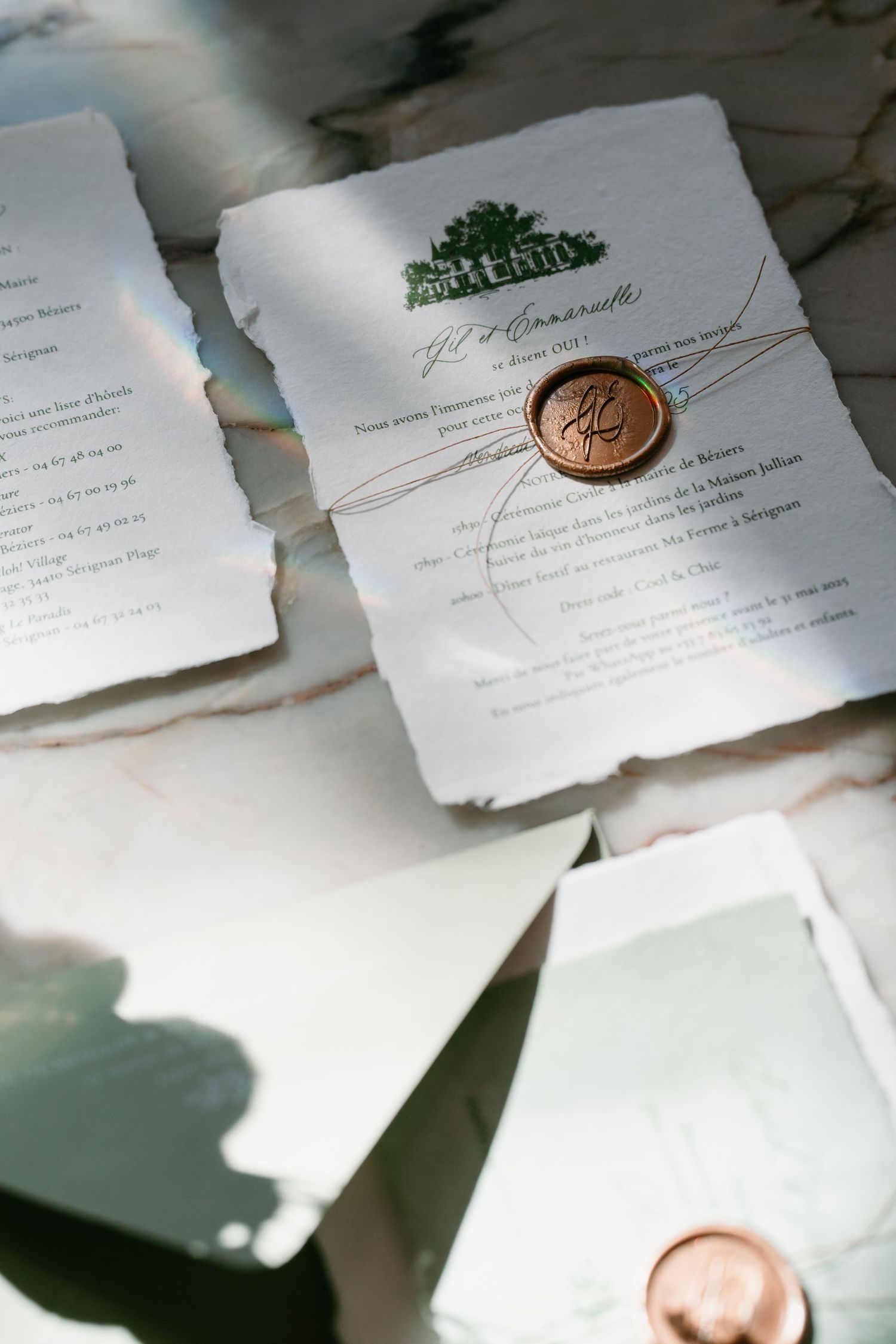 Elegant wedding invitations with torn edges and copper wax seals displayed on marble surface in natural light.