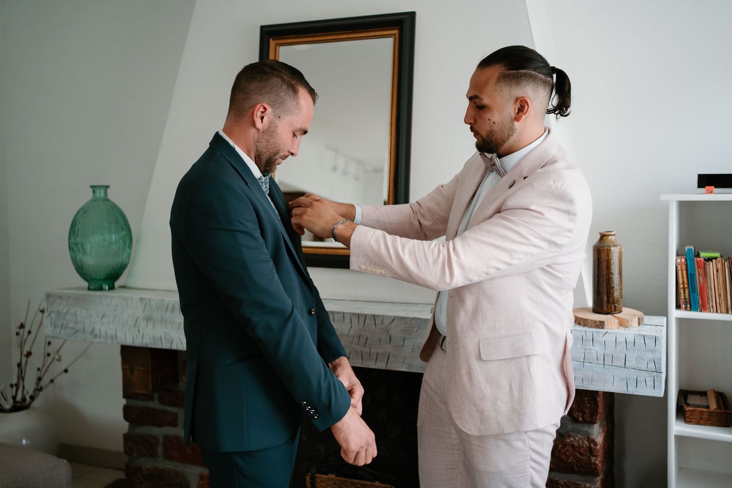 Two people in formal attire shake hands in an office setting with a white wall and decor in the background.