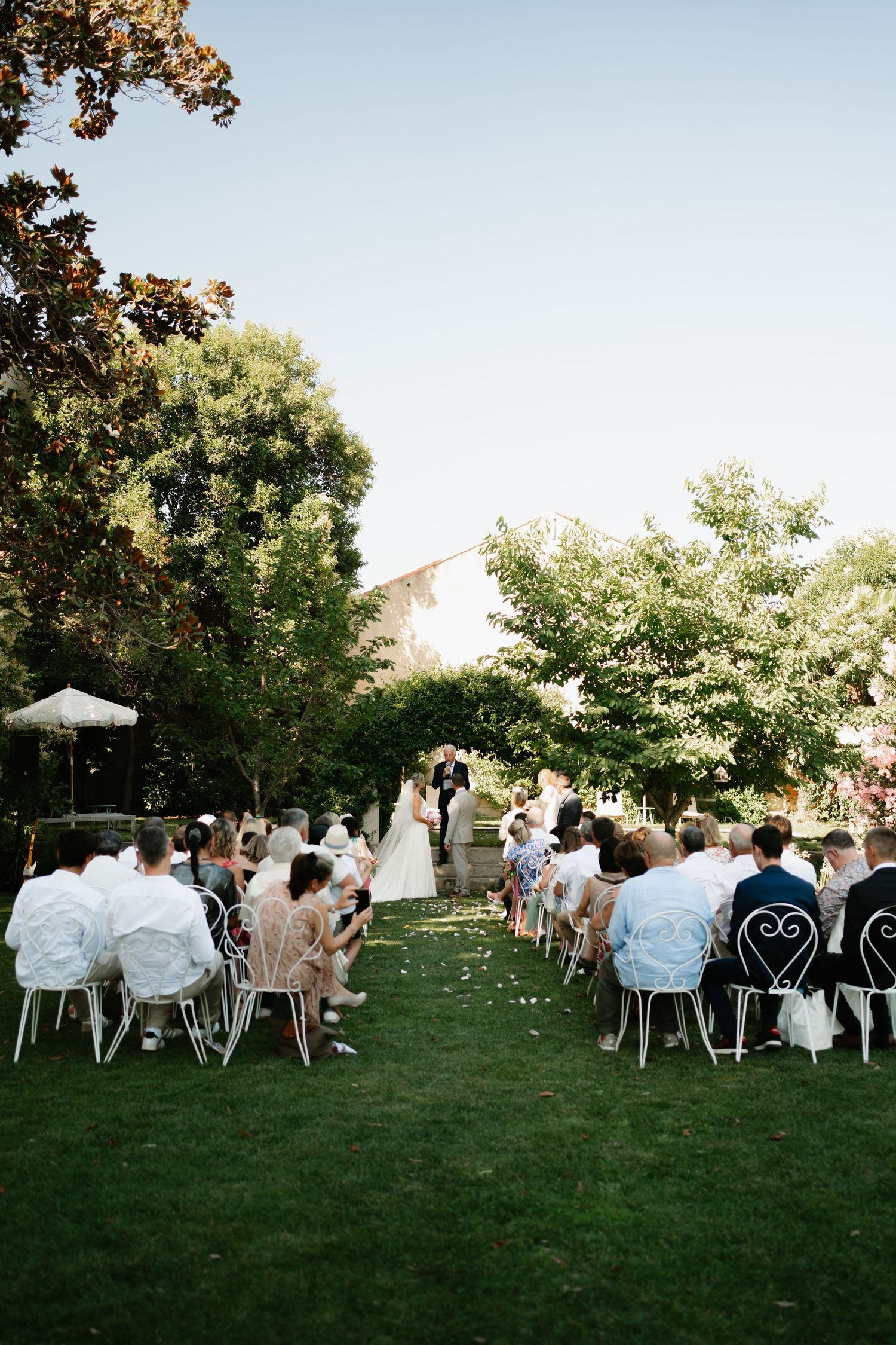 Guests seated at white chairs on a green lawn during an outdoor wedding reception at sunset.