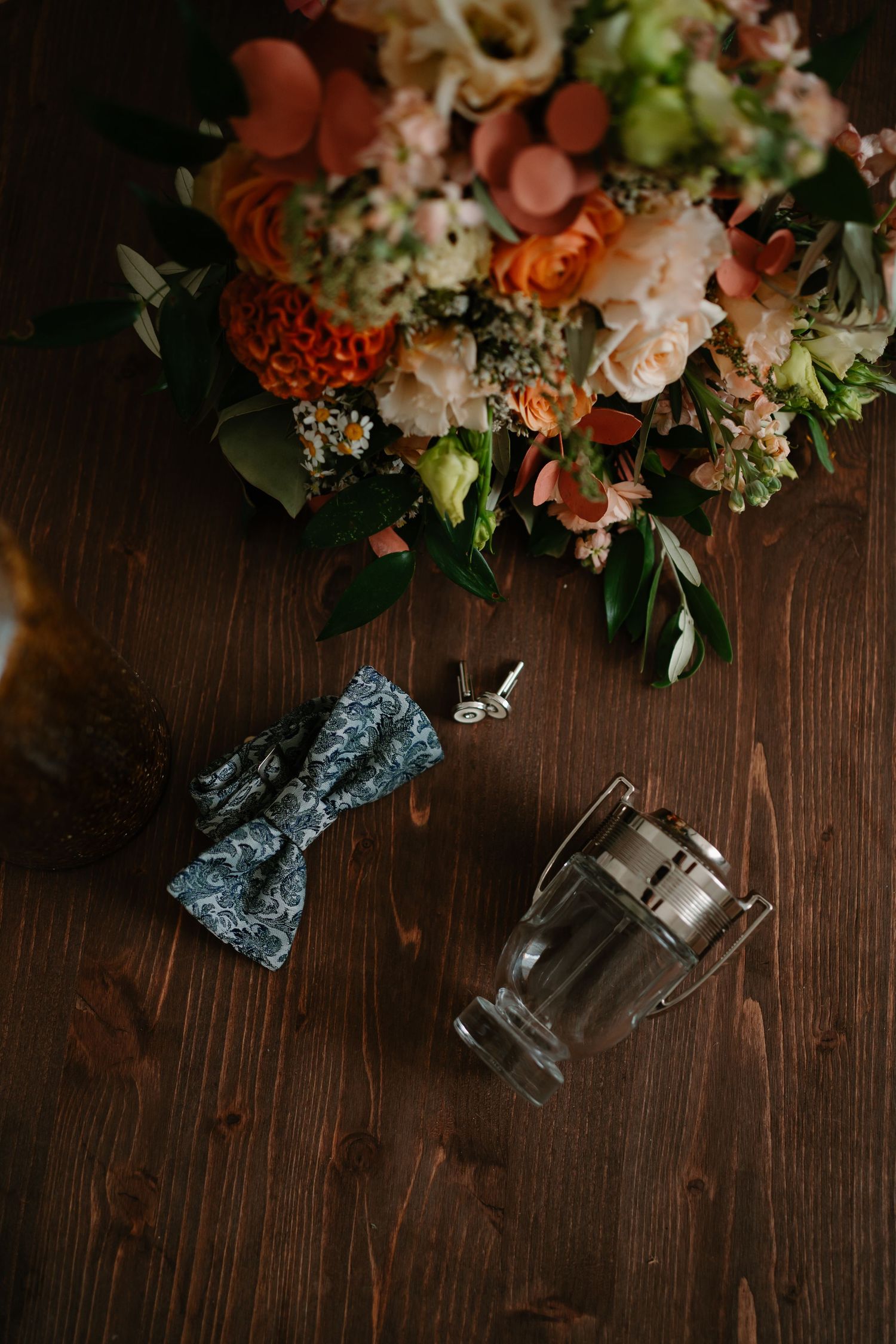 Fresh floral arrangement with coral roses and white blooms on dark wooden surface with vintage glass bottles.