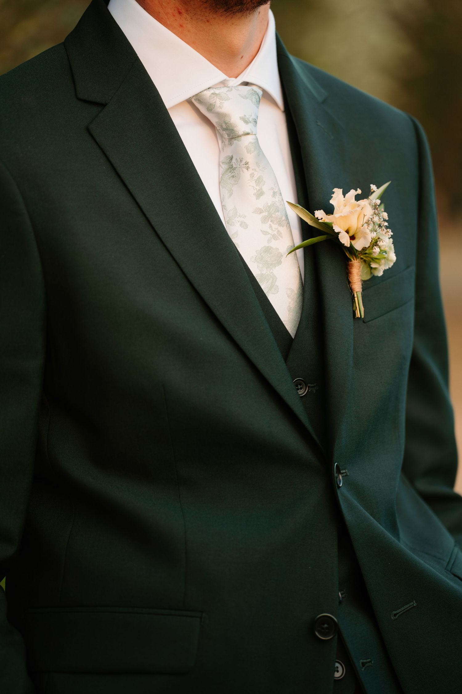 Close-up details of a formal black suit jacket with white dress shirt, tie and delicate floral boutonniere.