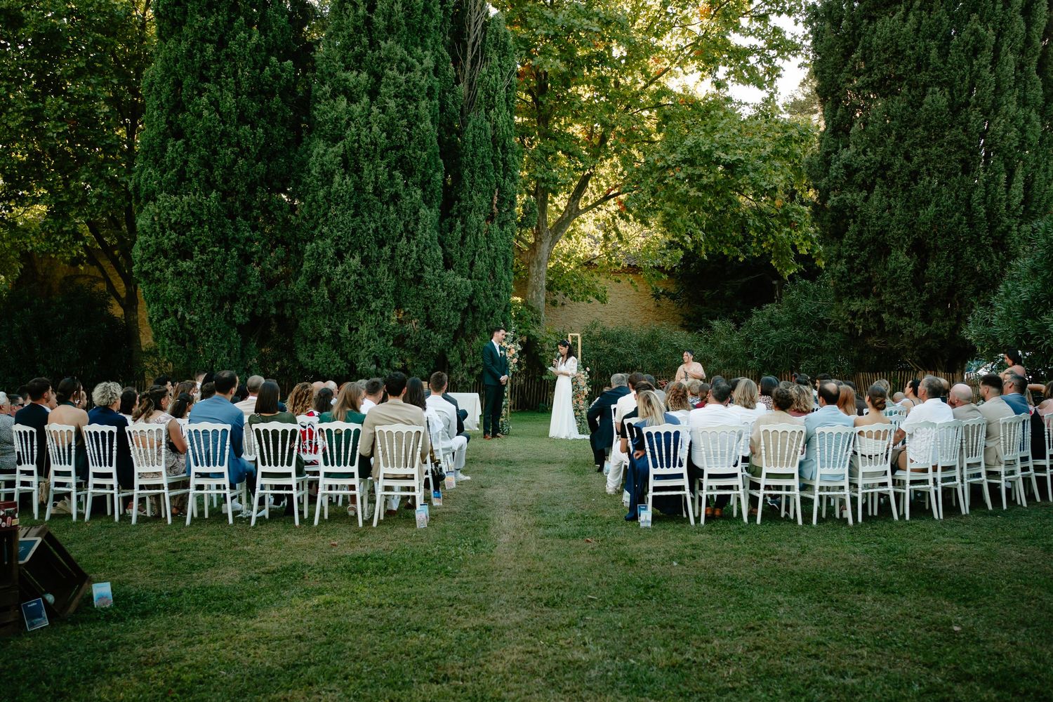 White chairs arranged in neat rows for an outdoor wedding ceremony with a tree-lined backdrop.