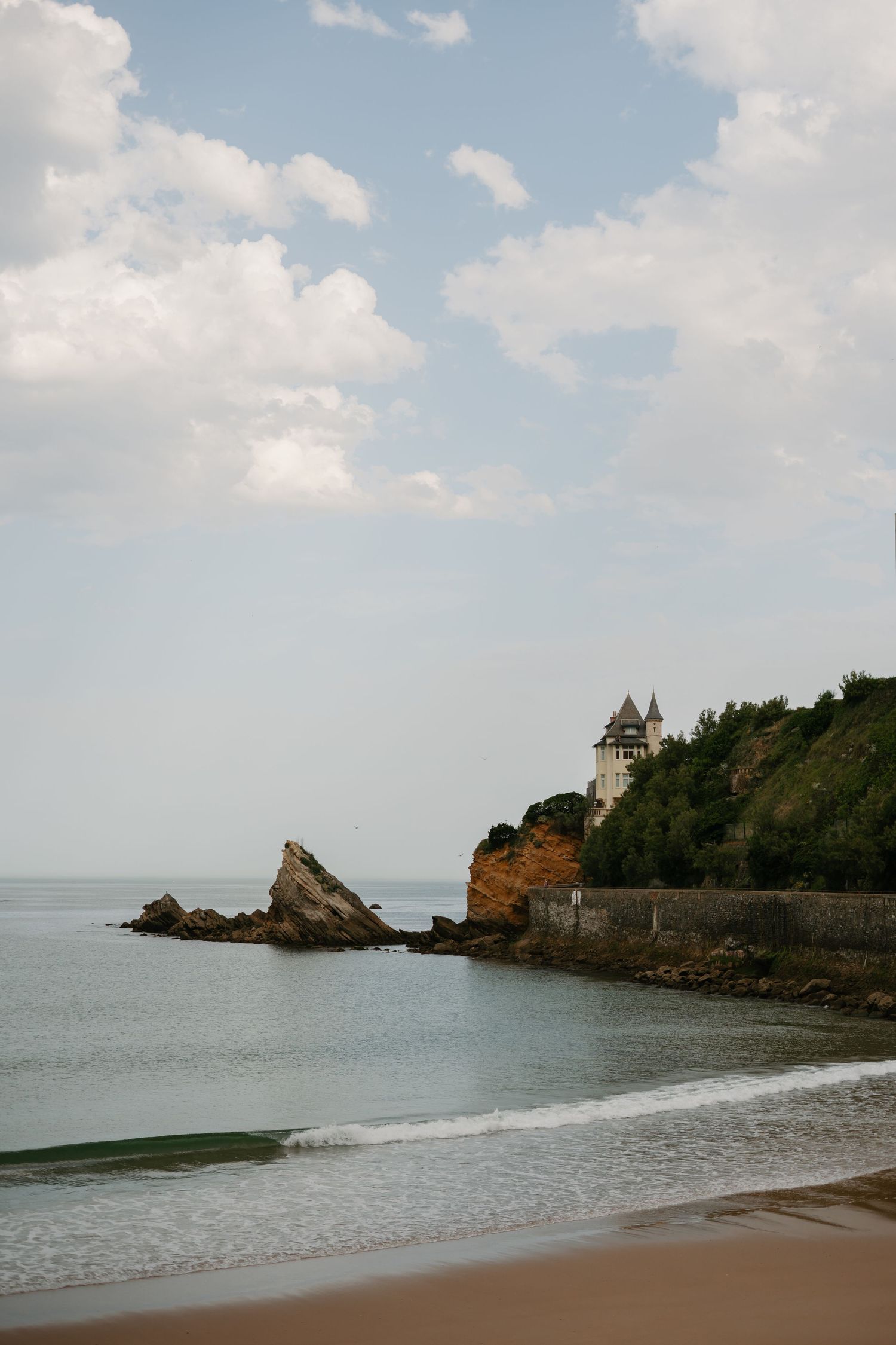 Scenic coastal view of a castle perched on rocky cliffs overlooking a sandy beach.