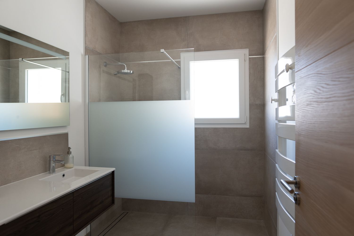 Modern bathroom interior with brown tile walls, white fixtures, and natural lighting through small window.