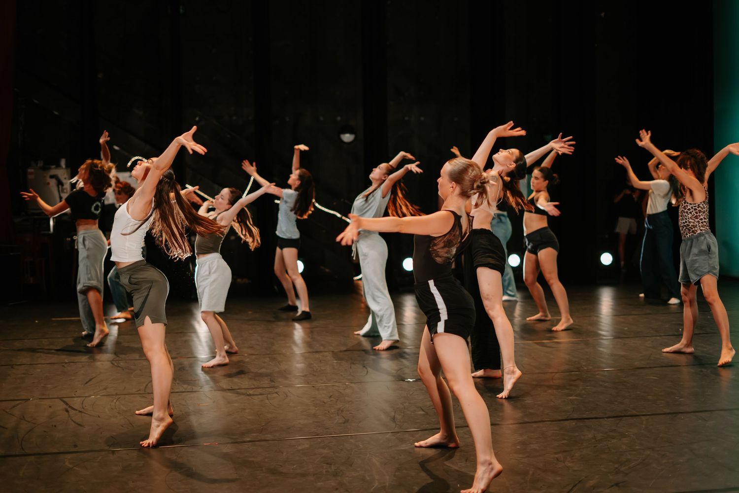 Contemporary dancers perform a dynamic sequence of movements on a dark stage during a modern dance performance.