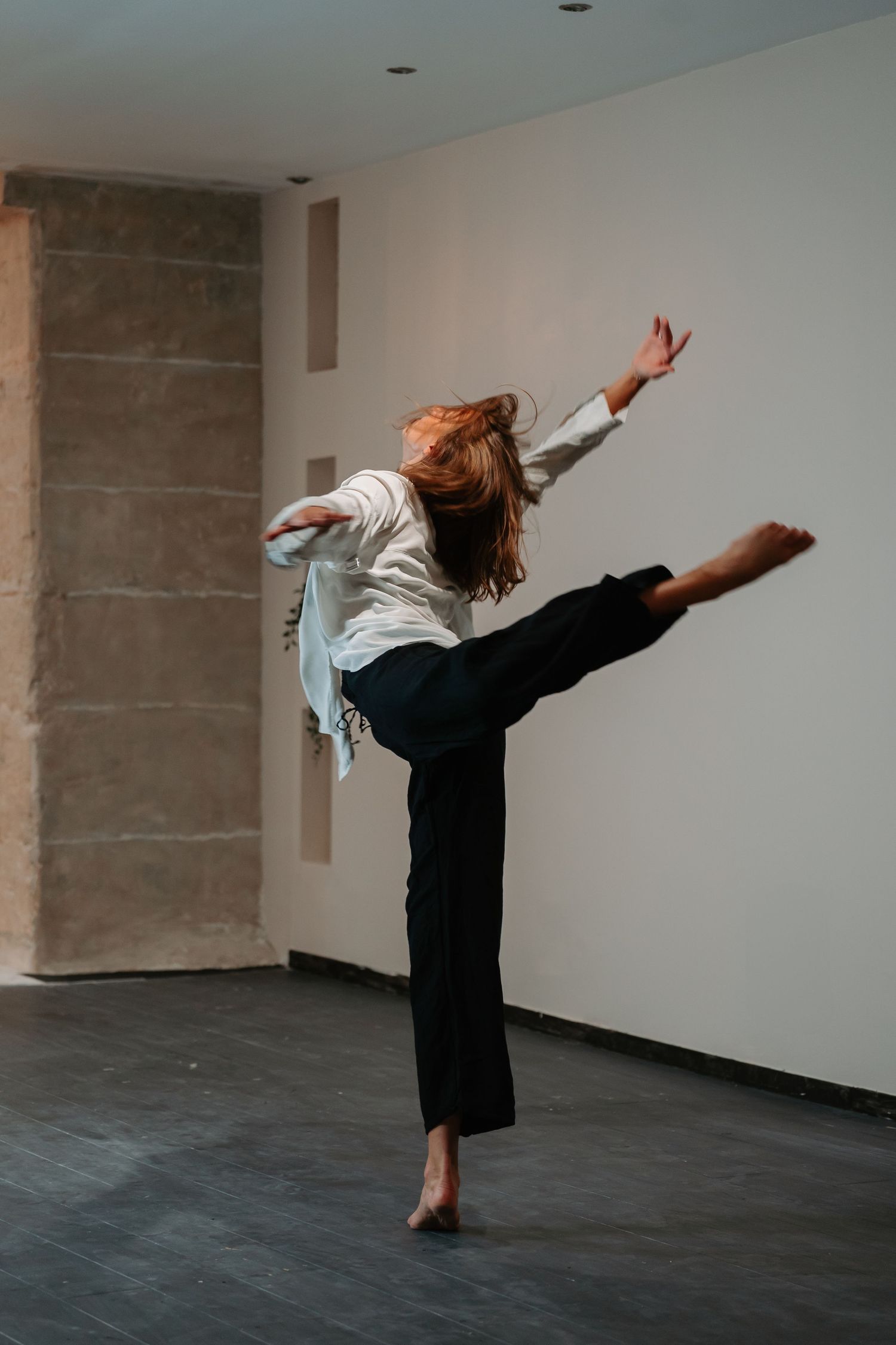 A dancer performs a dynamic sequence of expressive movements against a minimalist white and gray studio backdrop.