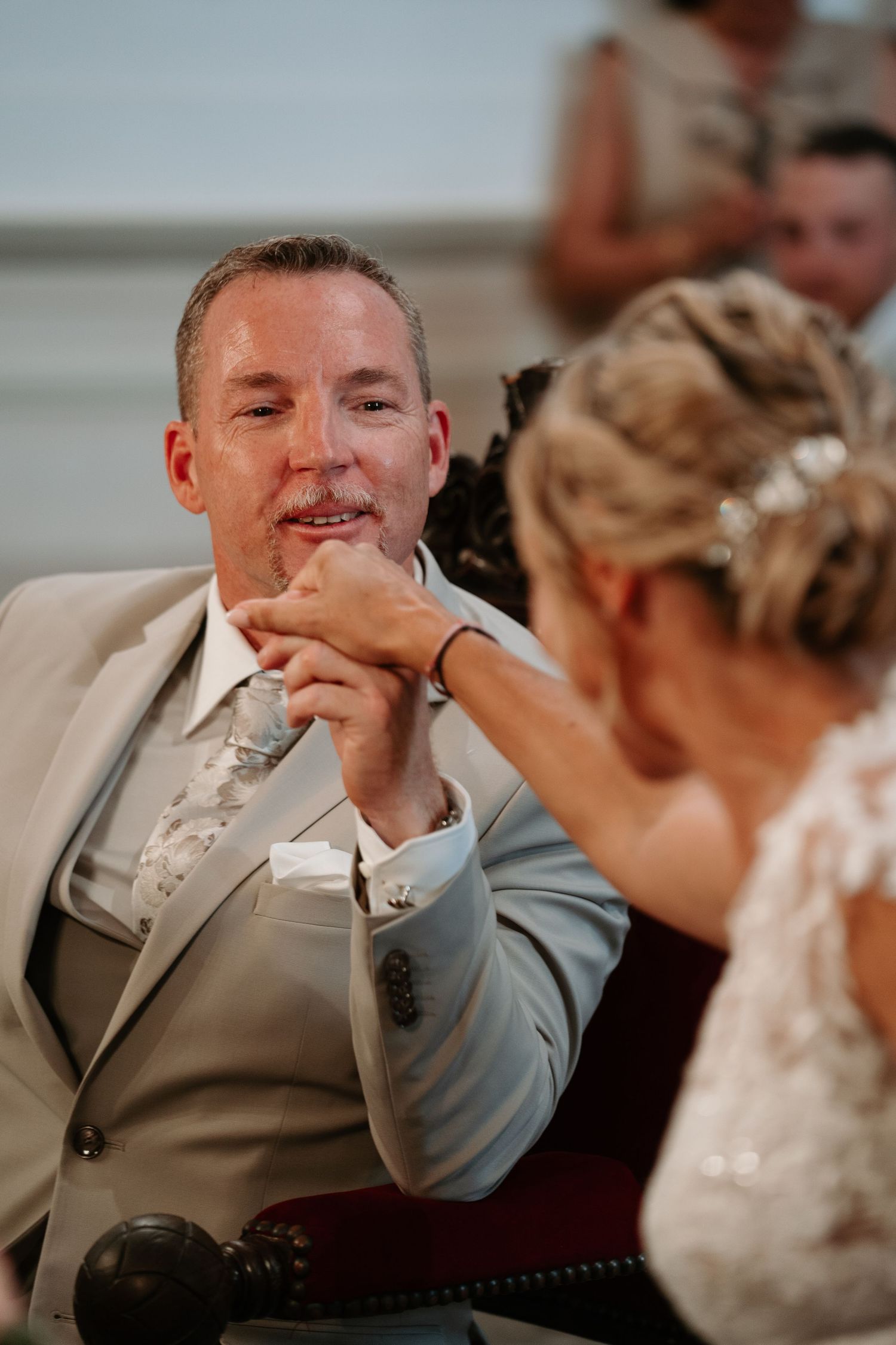 Wedding guest in a gray suit reacts emotionally during reception speeches with varying expressions of joy and laughter.