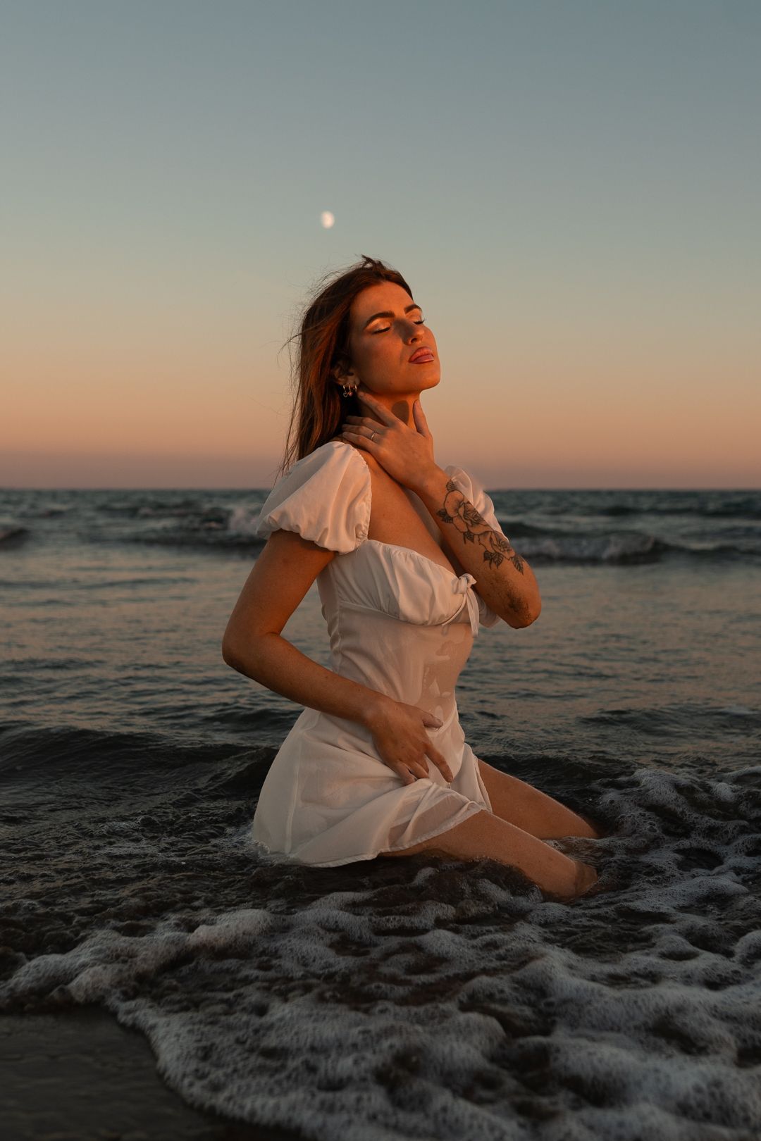 A woman in white poses expressively at sunset on a beach as waves crash around her in a series of artistic shots.