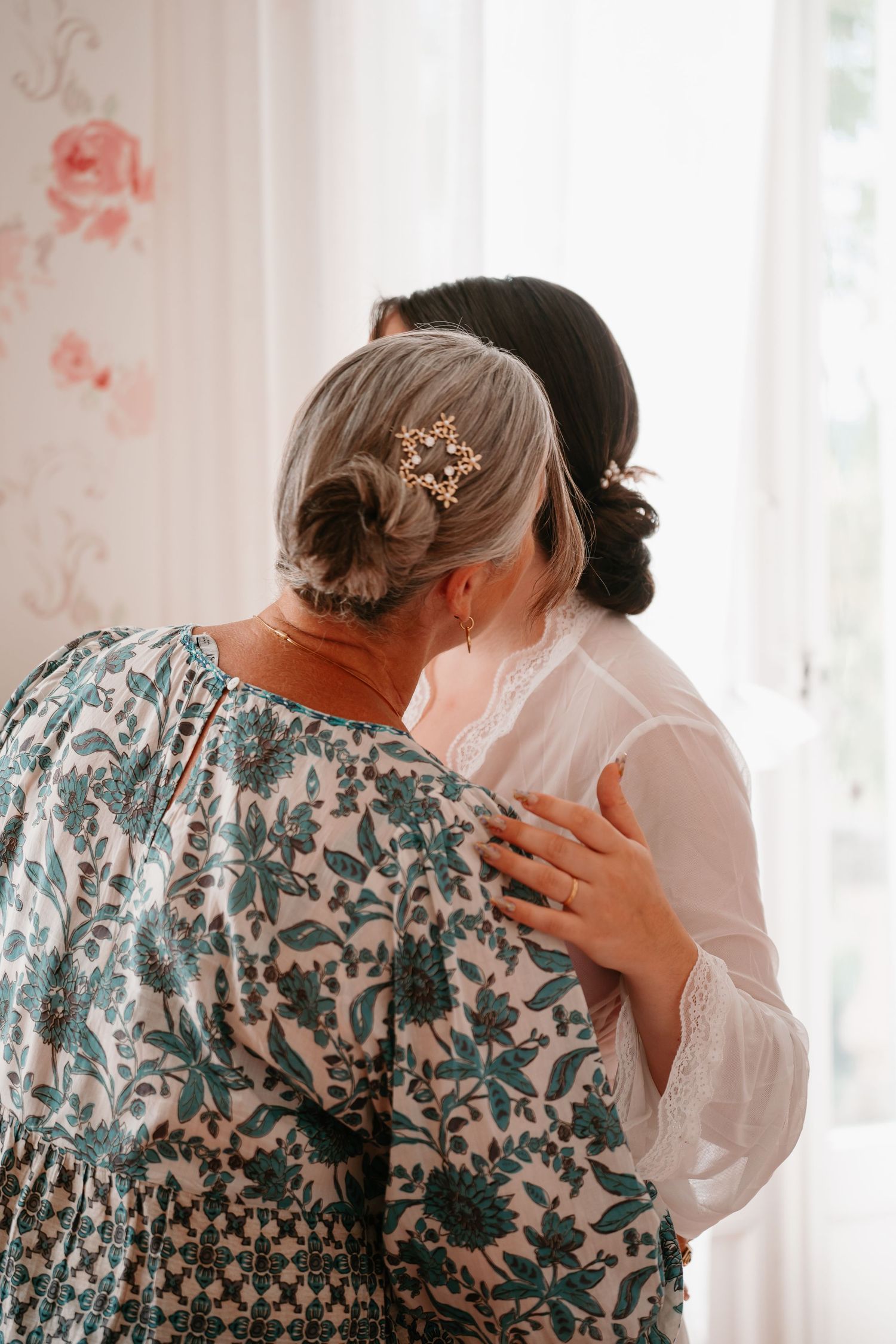 Two people embrace in a tender moment wearing white and floral patterned clothing against a light background.