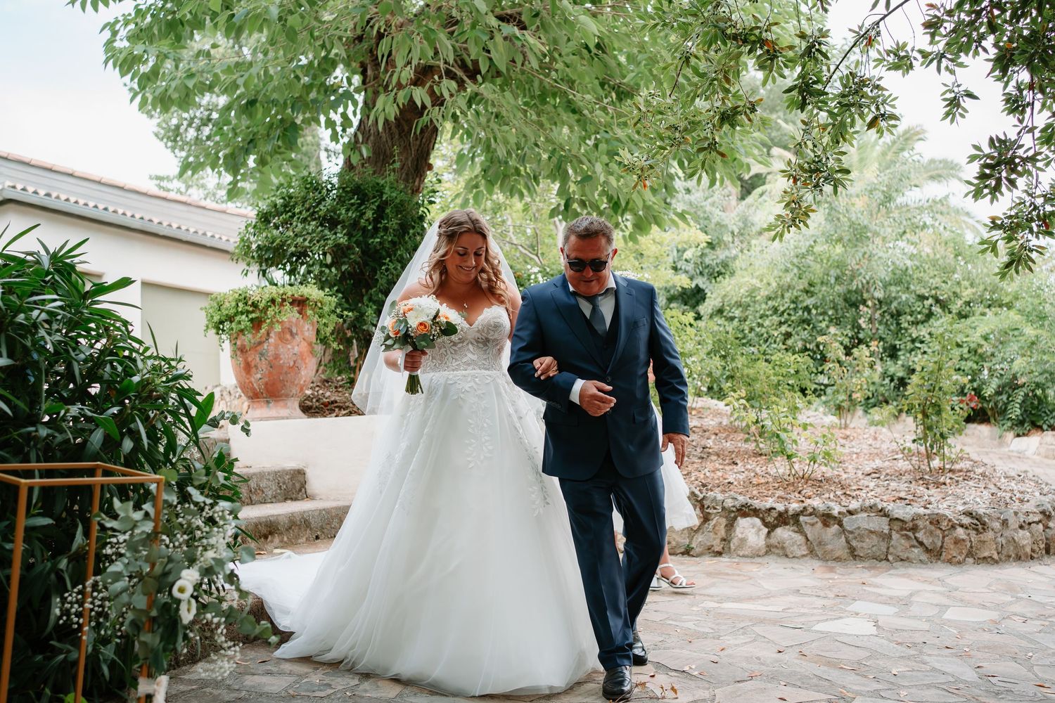 A couple in wedding attire walks together through a lush garden path on their special day.