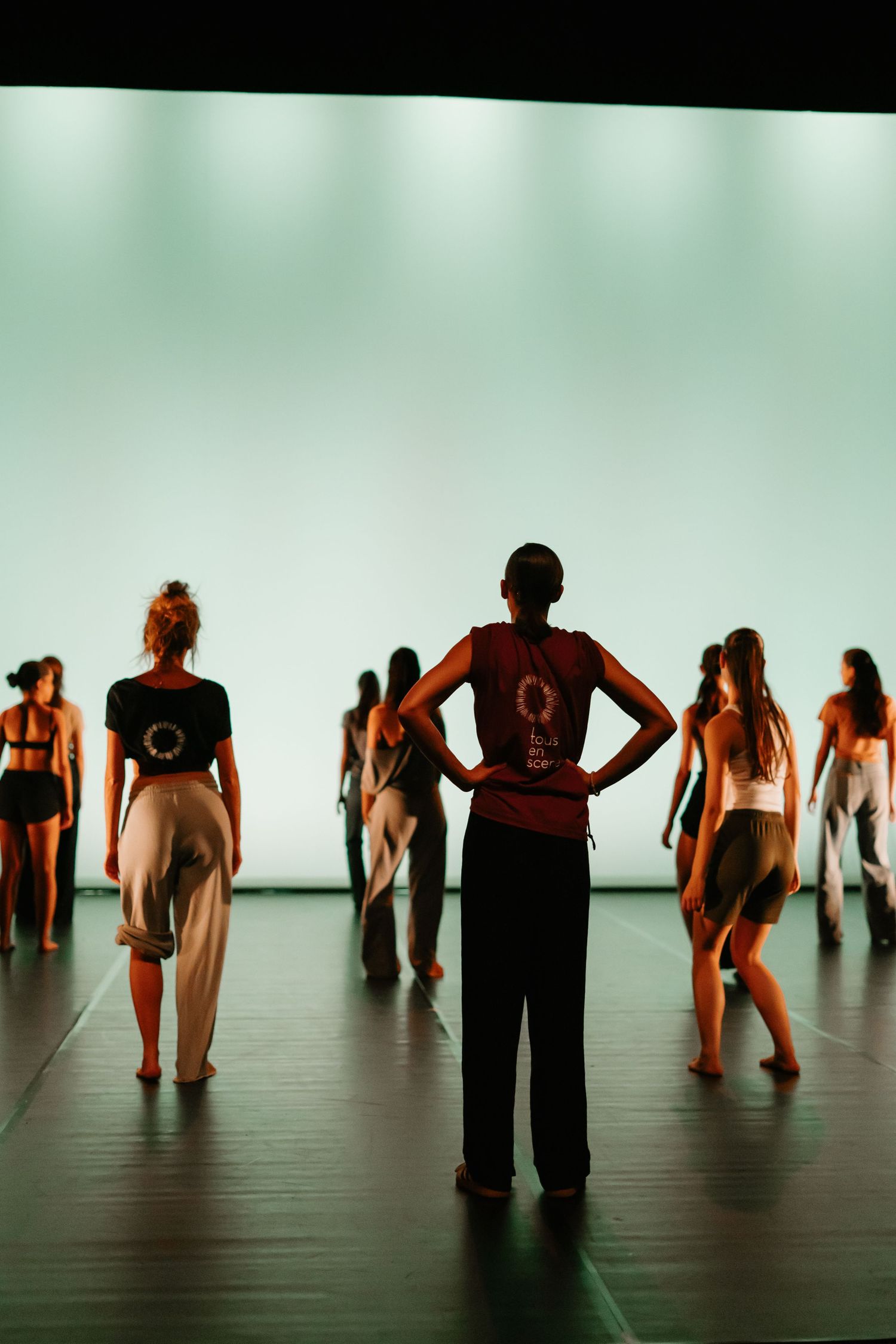 Dancers in silhouette perform on a minimalist stage with turquoise lighting creating a dramatic artistic effect.
