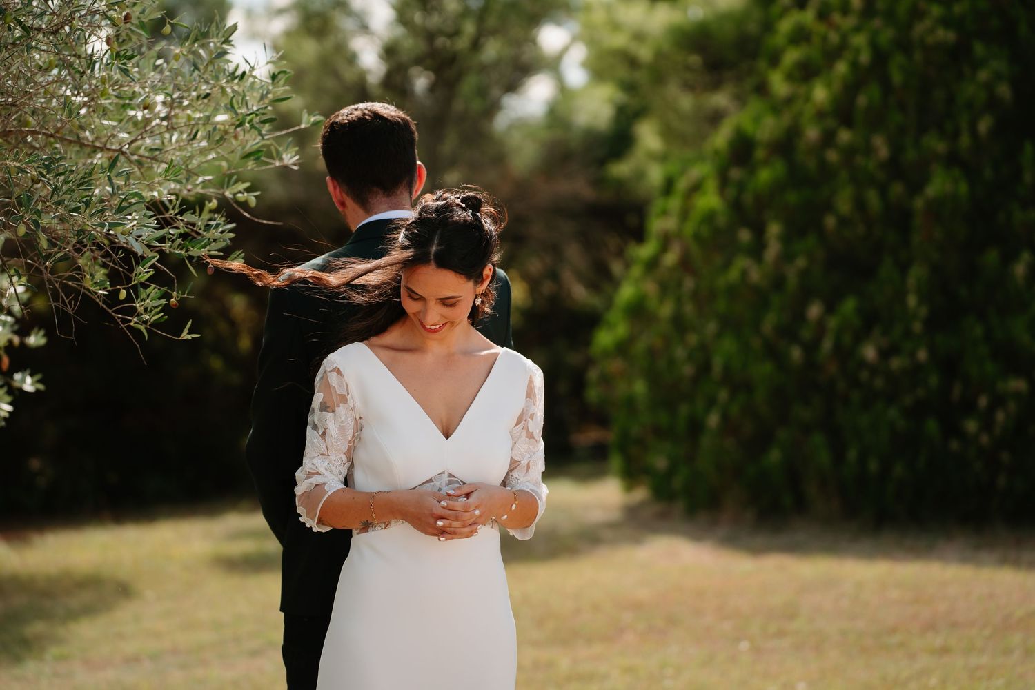 A couple in wedding attire shares an intimate moment in a sunlit garden setting with lush greenery.