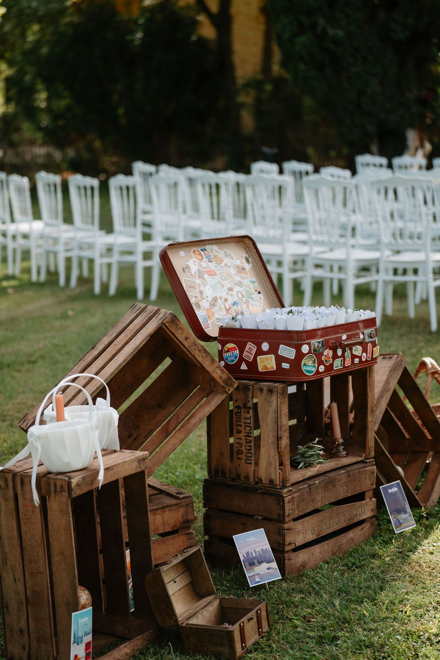 Rustic wooden crates with floral cushions arranged as outdoor seating with white chairs in the background at a wedding venue.