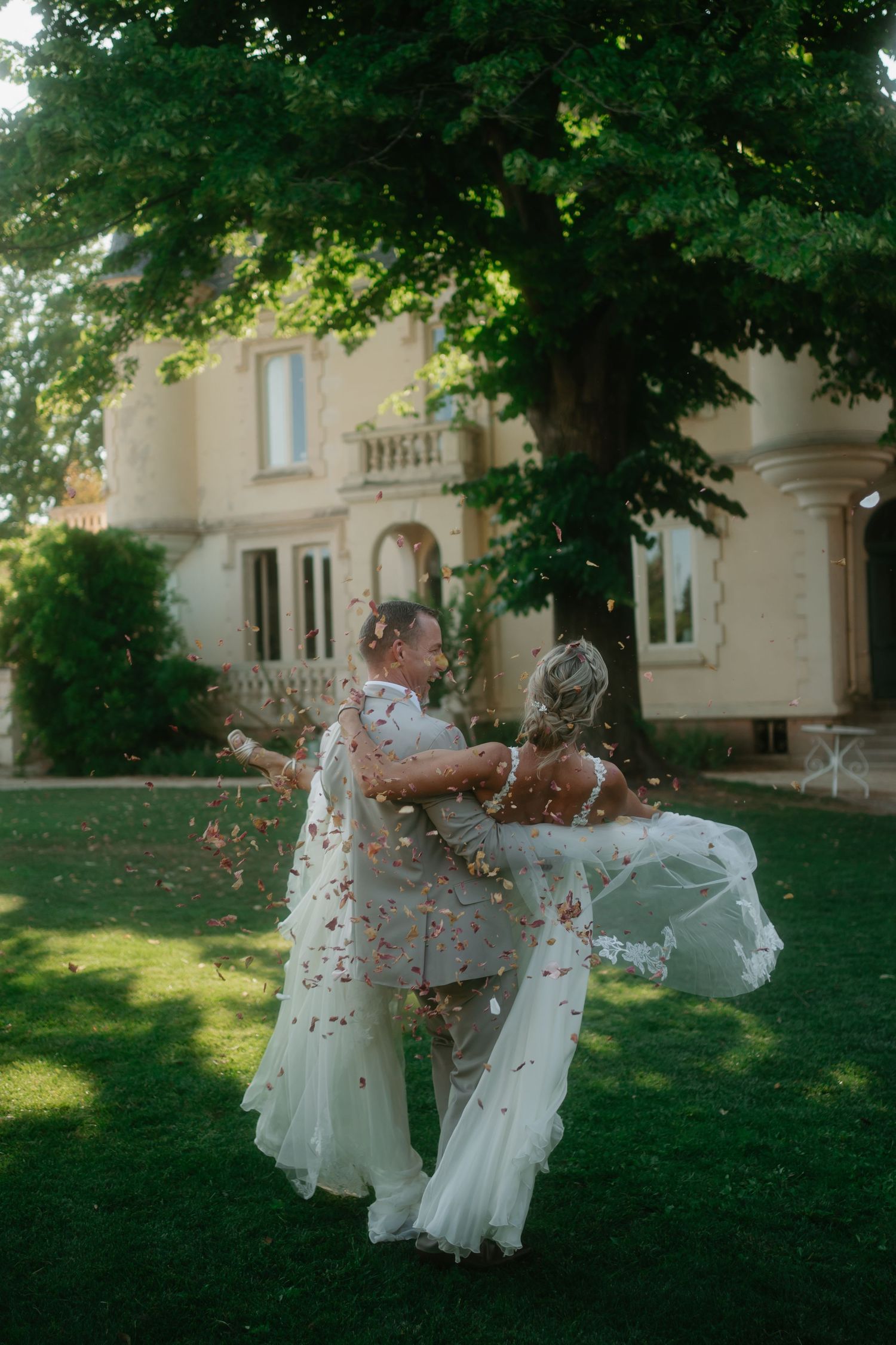 A joyful moment captured in front of an elegant mansion as two people in white dresses dance and celebrate on the lawn.