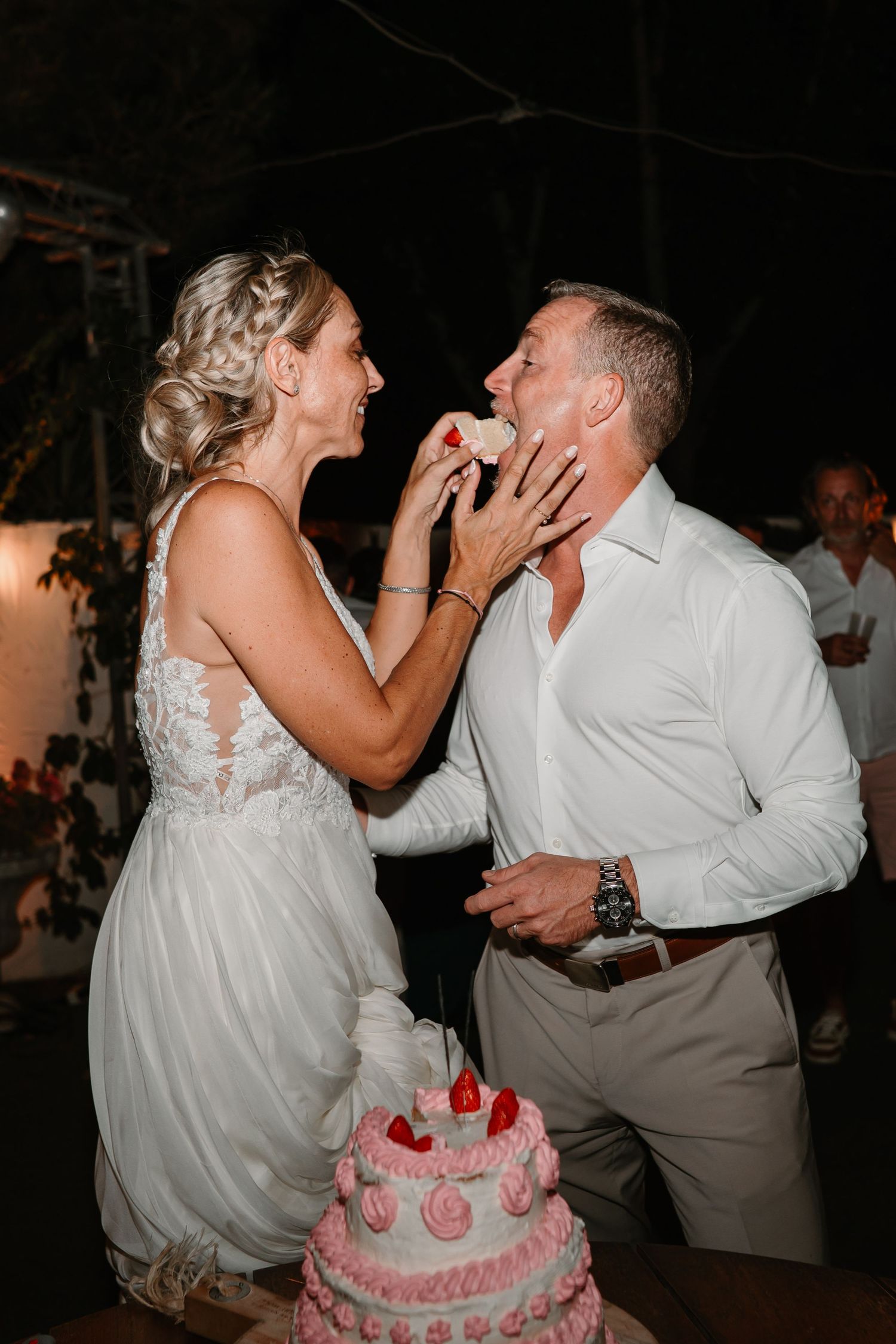 A couple shares a playful moment feeding each other wedding cake during their reception celebration.