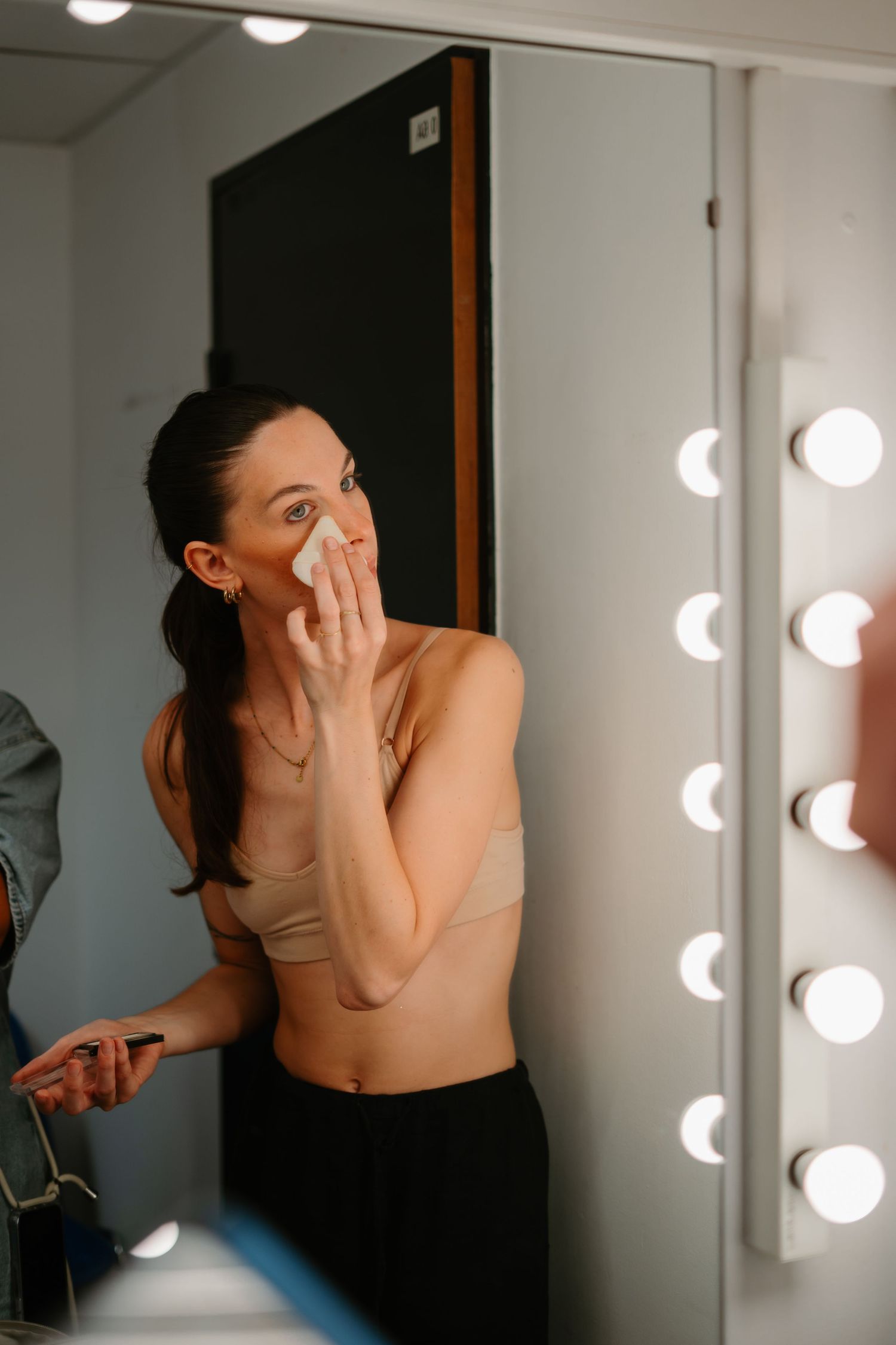 A series of artistic portraits showing someone in a black top covering their face near a vanity mirror with round lights.