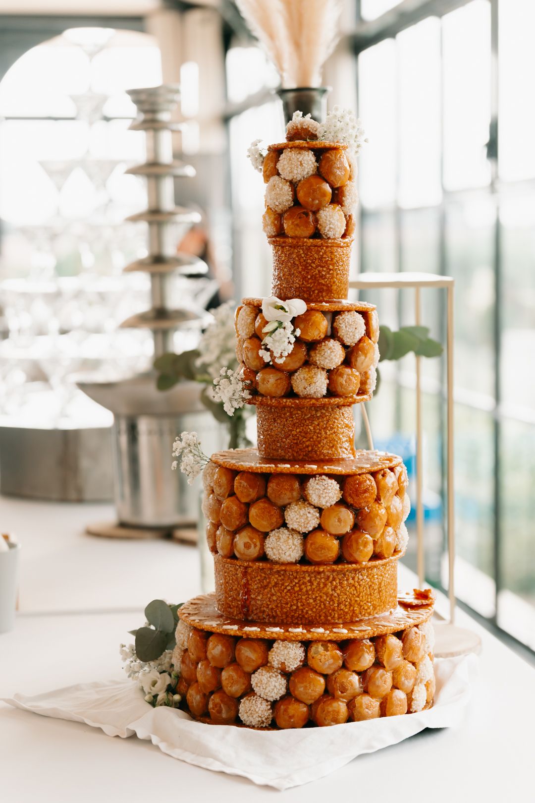 Elegant tiered wedding cake decorated with cream puffs and gold accents on a white display stand.