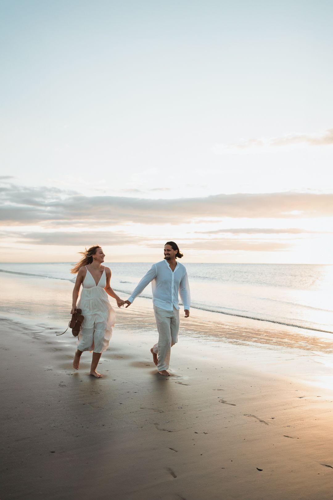 Couple strolling hand in hand along beach shoreline at sunset.