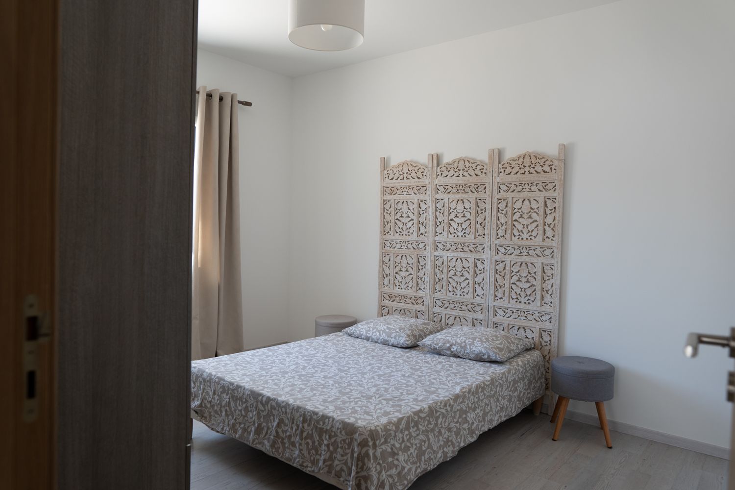 Cozy bedroom interior with white walls, decorative headboard, and brown curtains in a modern apartment setting.