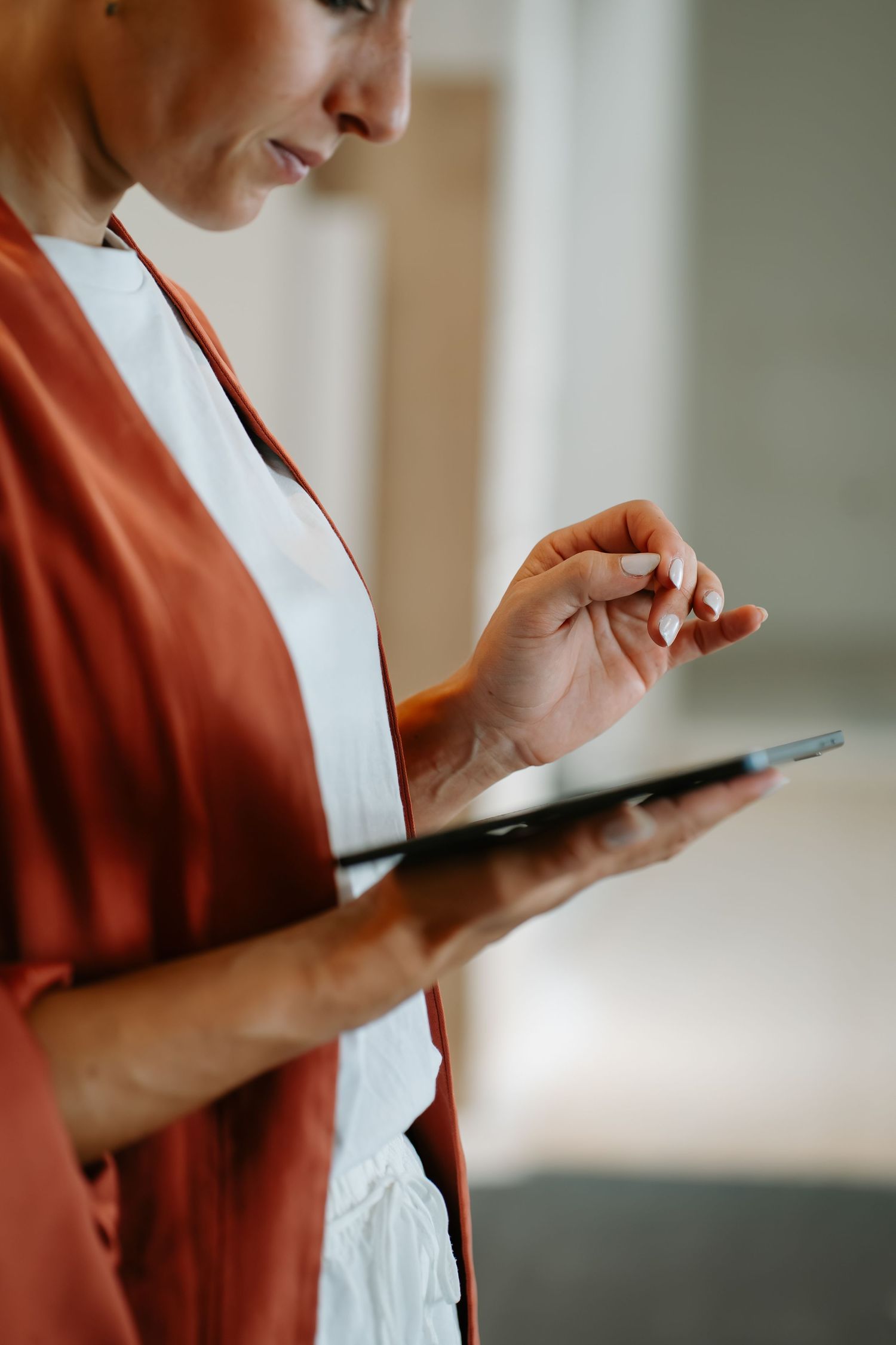 Person in a rust-colored cardigan using a digital tablet device in soft natural lighting.