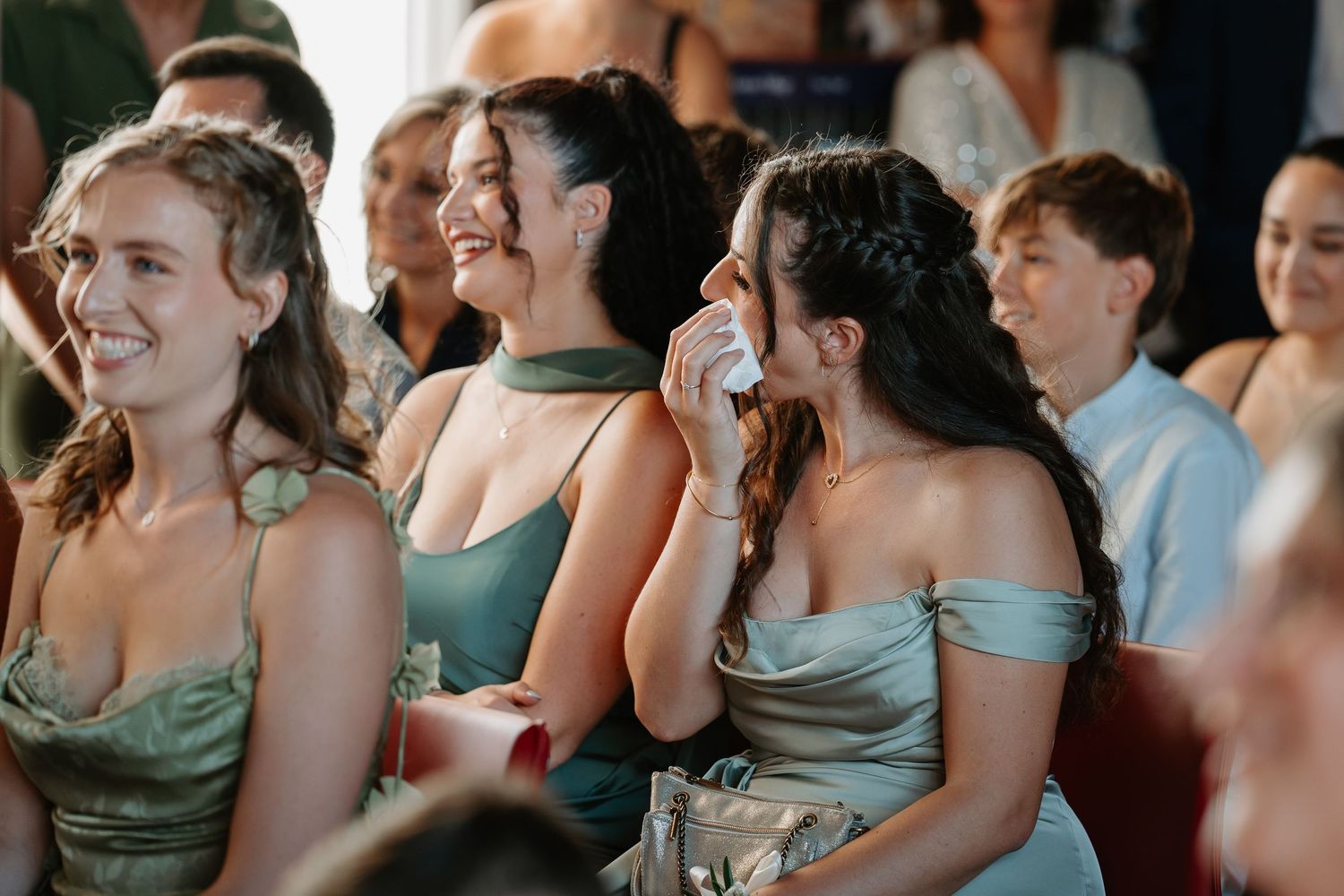 Wedding guests in sage green bridesmaid dresses share emotional reactions during a special moment at the ceremony.