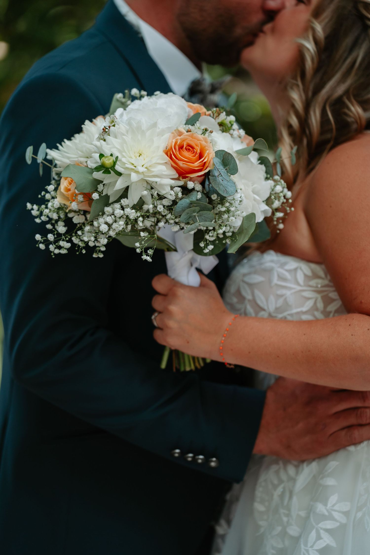 A wedding bouquet with white chrysanthemums, peach roses and baby's breath is held during an intimate moment.