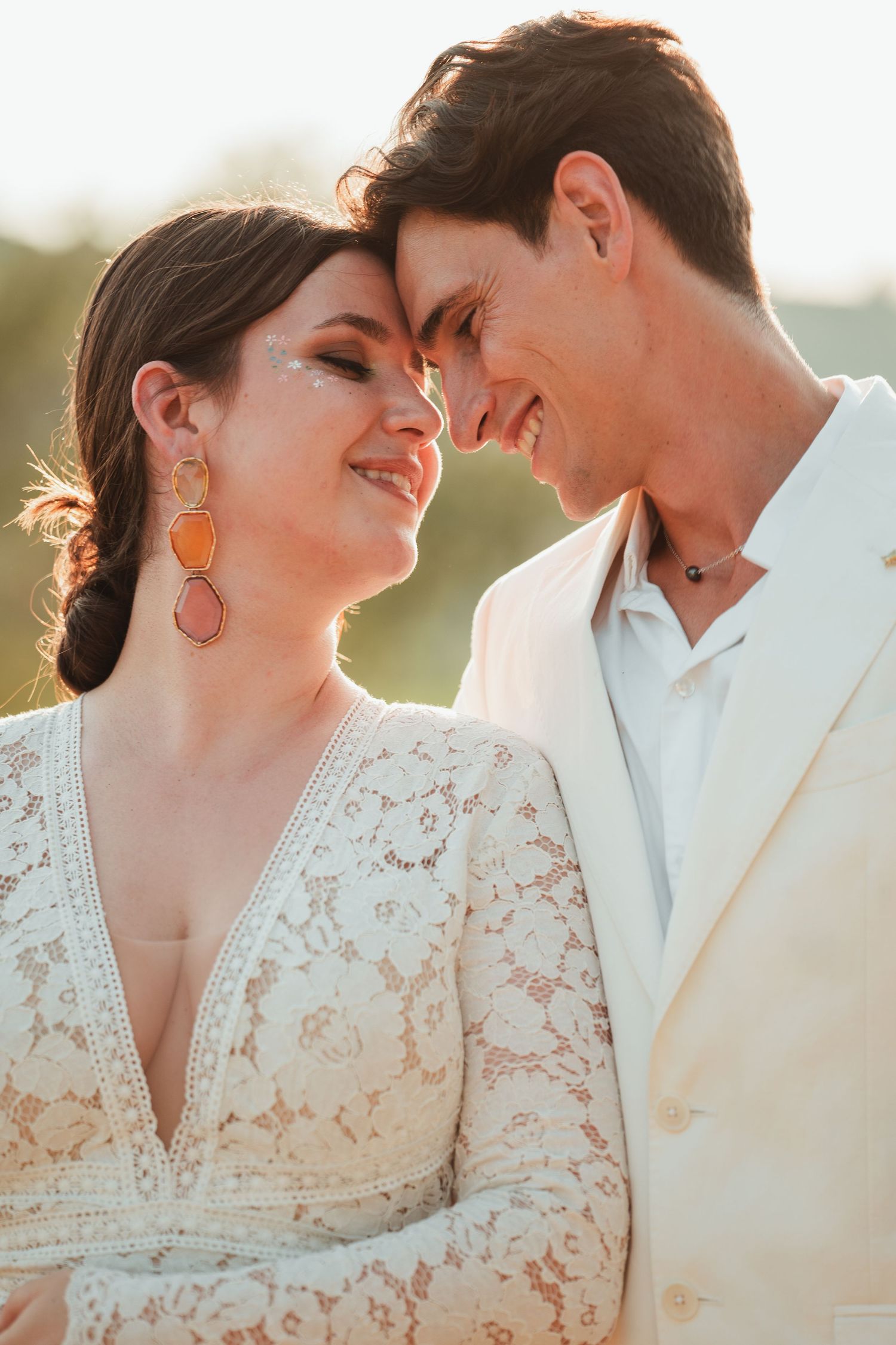 A couple in wedding attire share intimate moments at sunset, with the bride wearing a delicate lace dress.