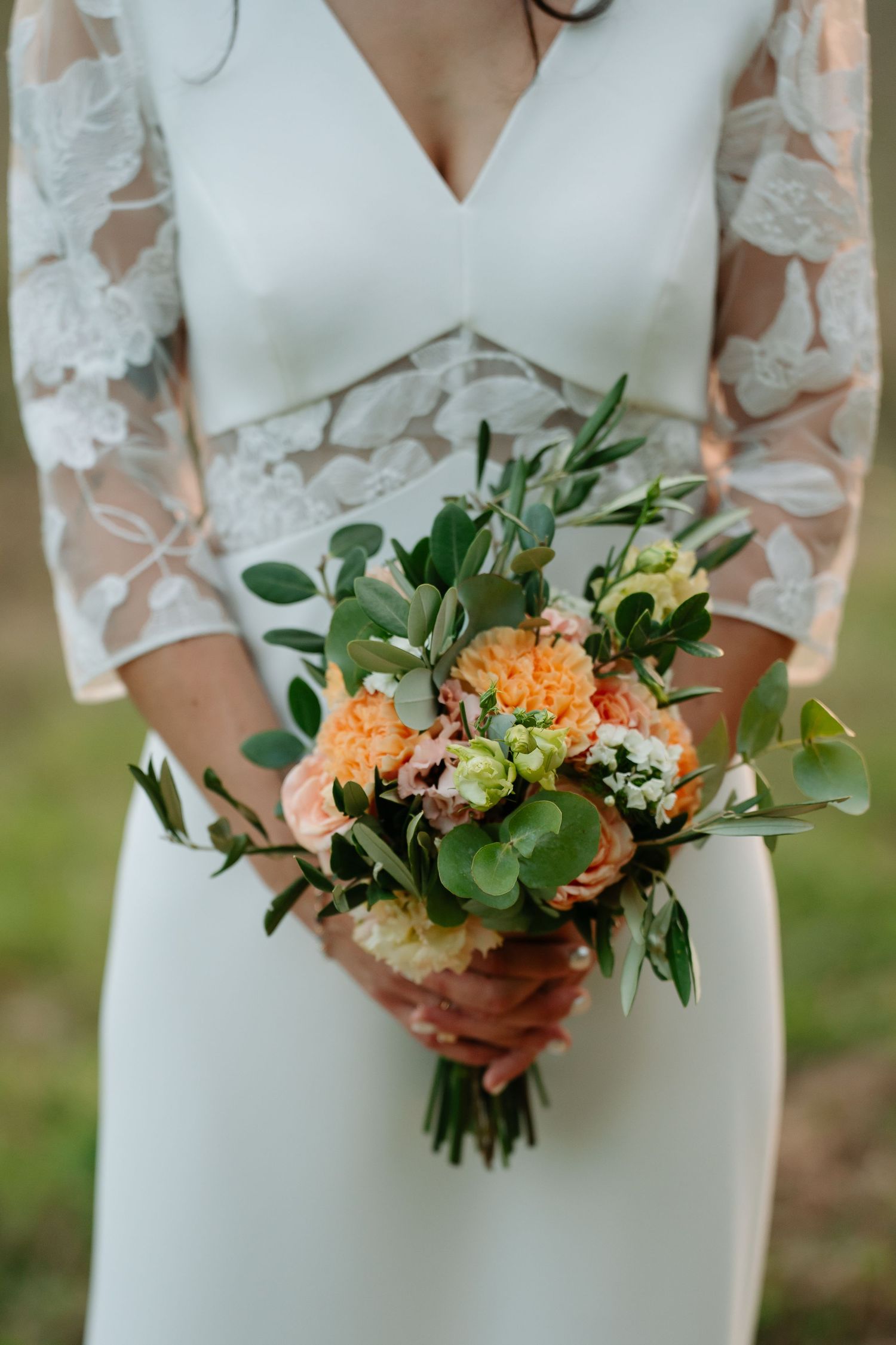 Wedding bouquet with peach-colored carnations, green eucalyptus leaves and delicate white lace sleeves in frame.