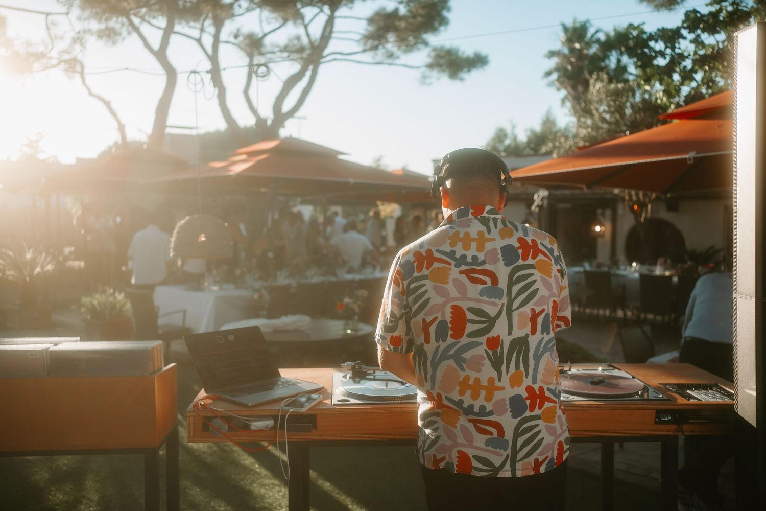 A collection of outdoor dining tables with orange umbrellas at a restaurant patio during golden hour sunset.