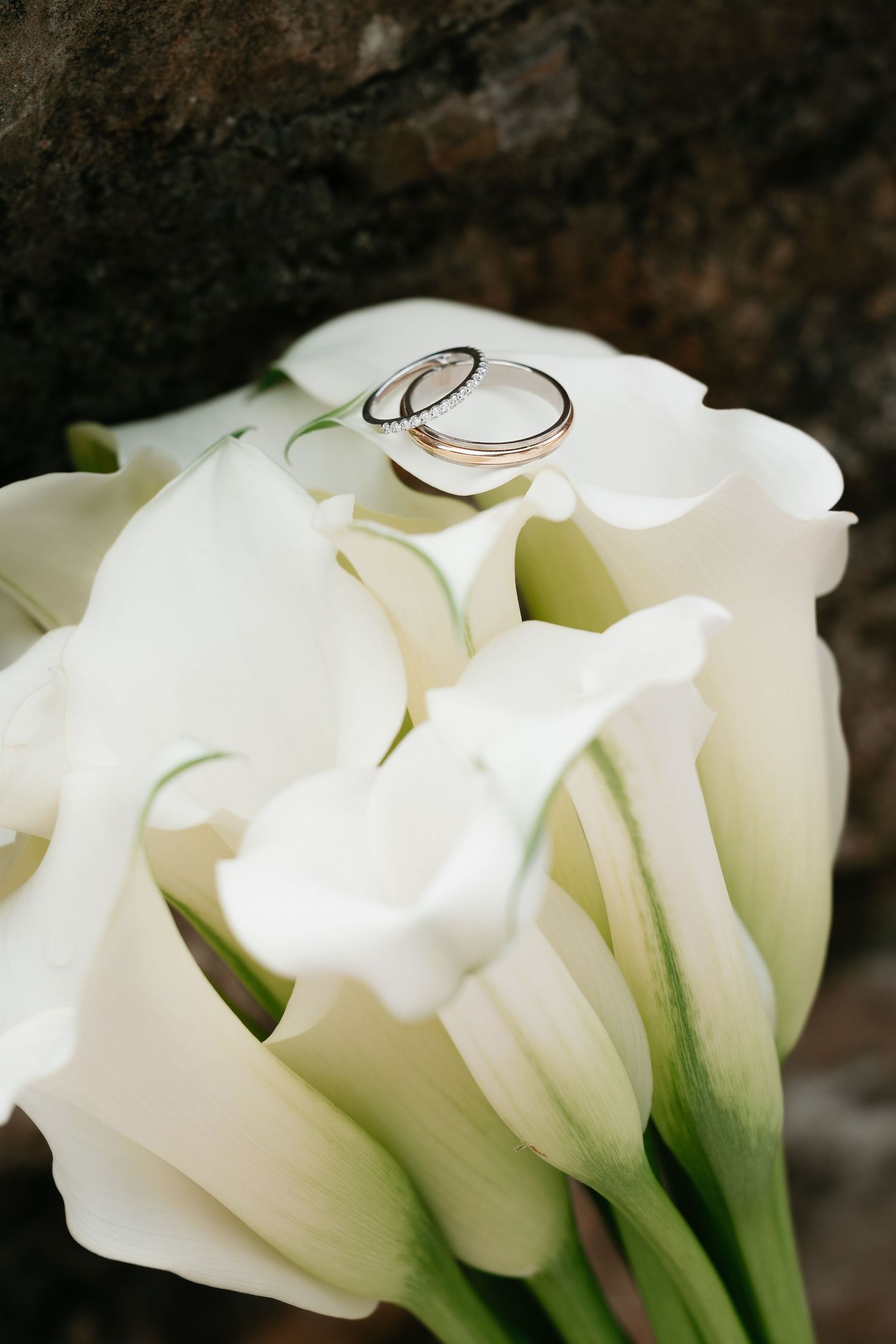 Two wedding rings resting on a bouquet of white calla lilies, symbolizing love and commitment.