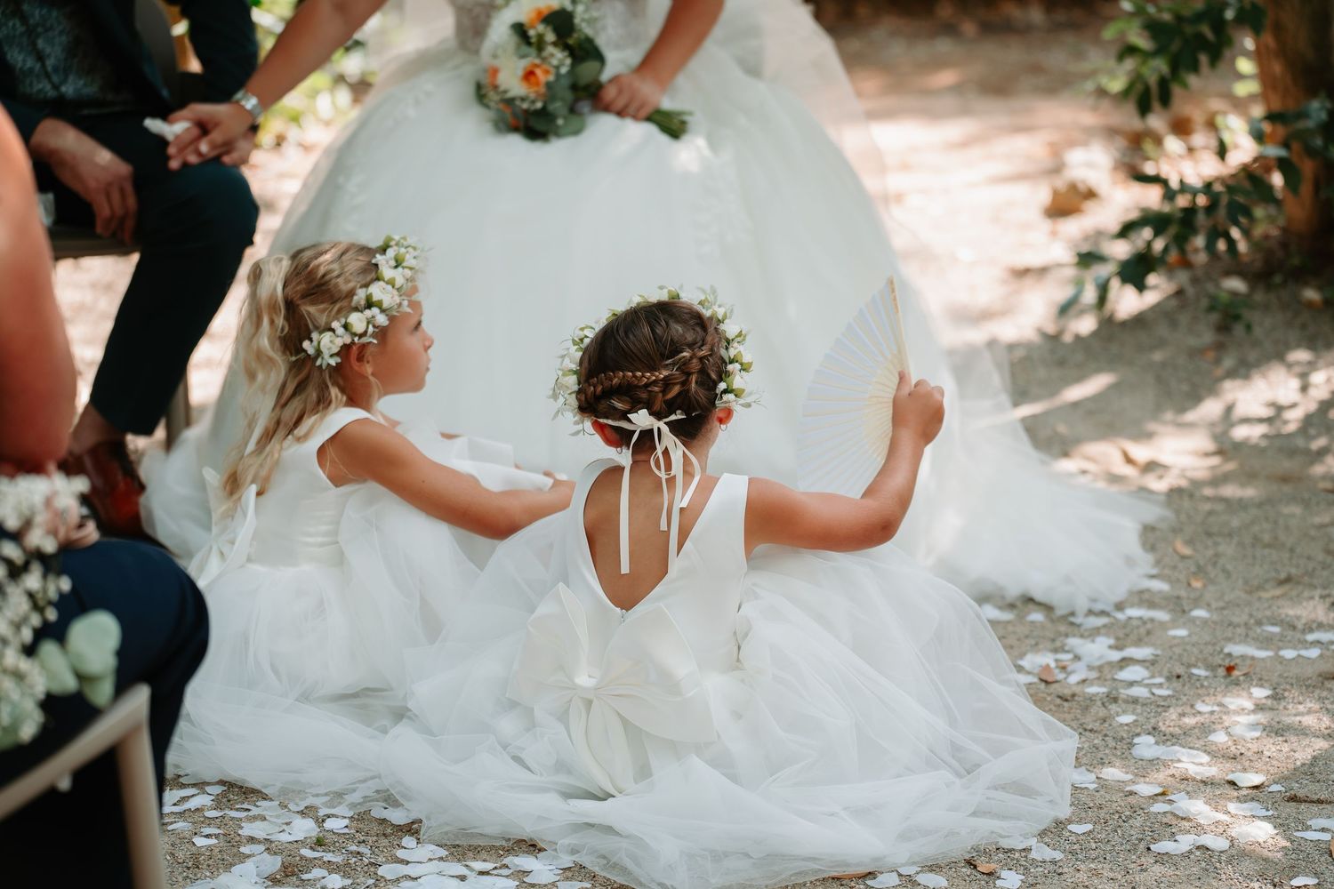 A bride in a flowing white wedding dress twirls and dances joyfully in dappled sunlight outdoors.